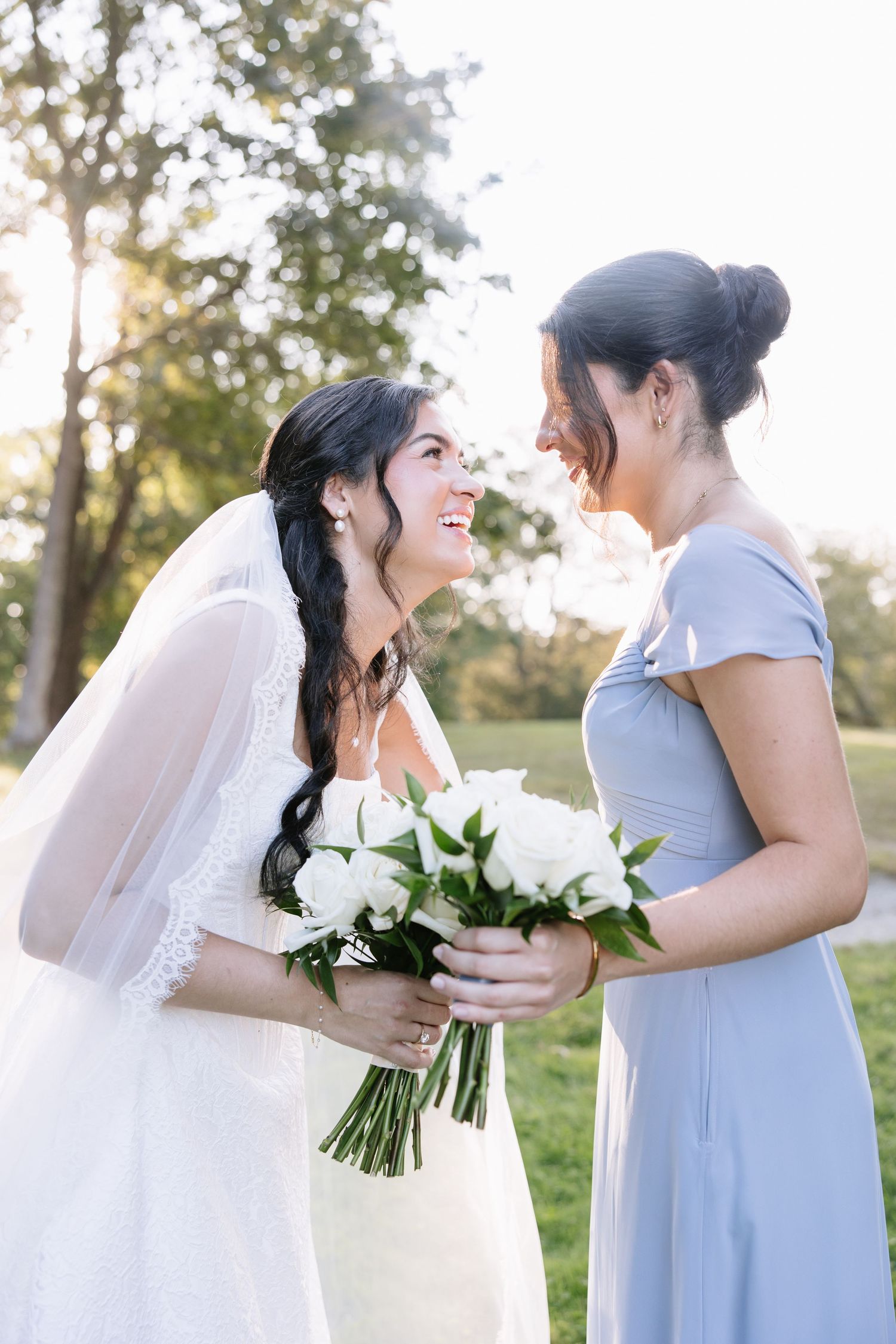 Wedding party members in white and grey dresses share joyful moments with white bouquets.