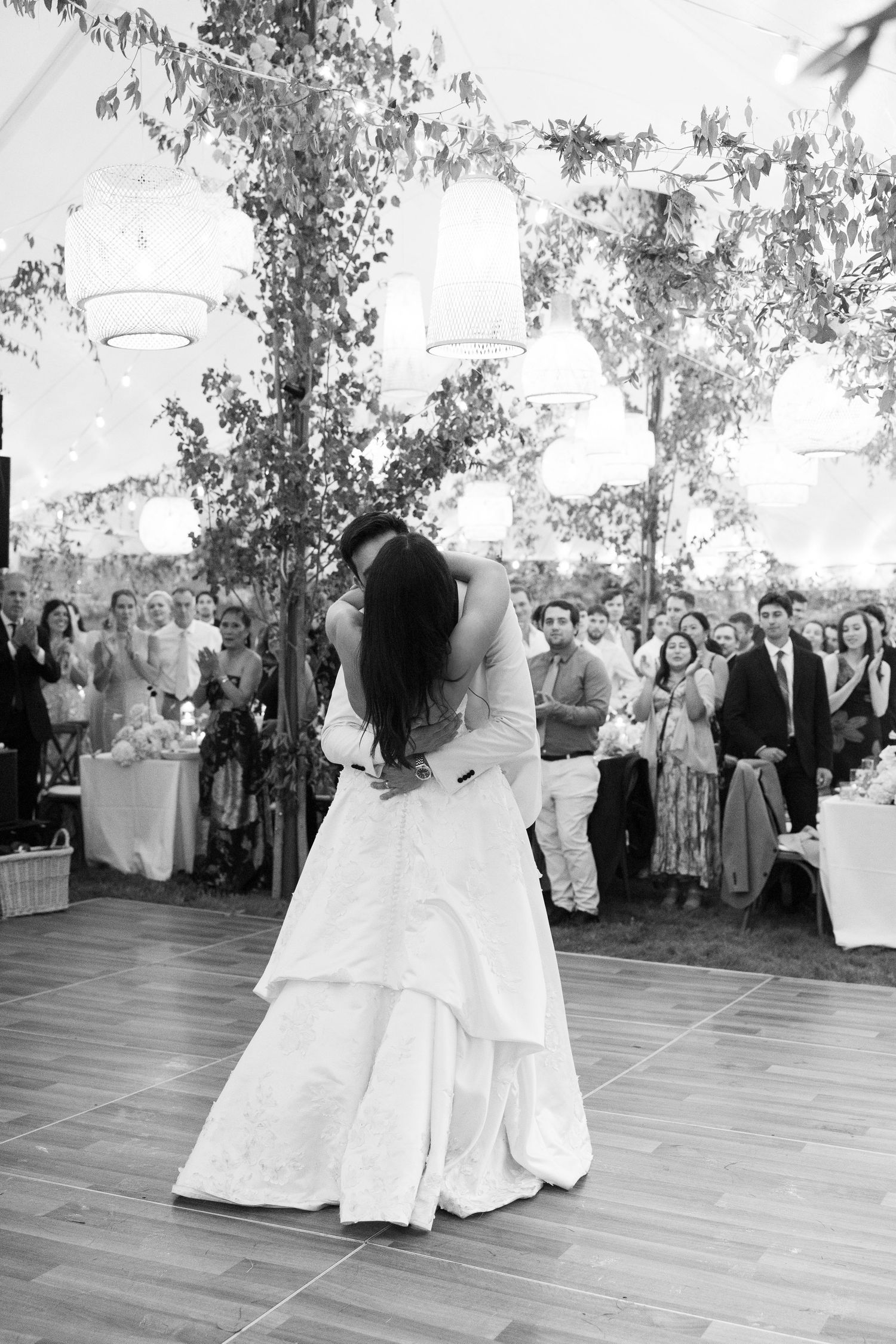 Bride and groom share romantic first dance kiss before guests at outdoor wedding reception.