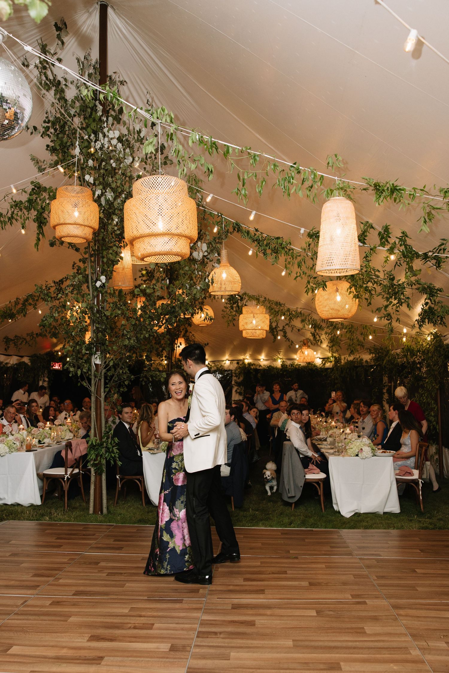 Couple shares first dance under glowing rattan lanterns and greenery in an elegant tented wedding reception.