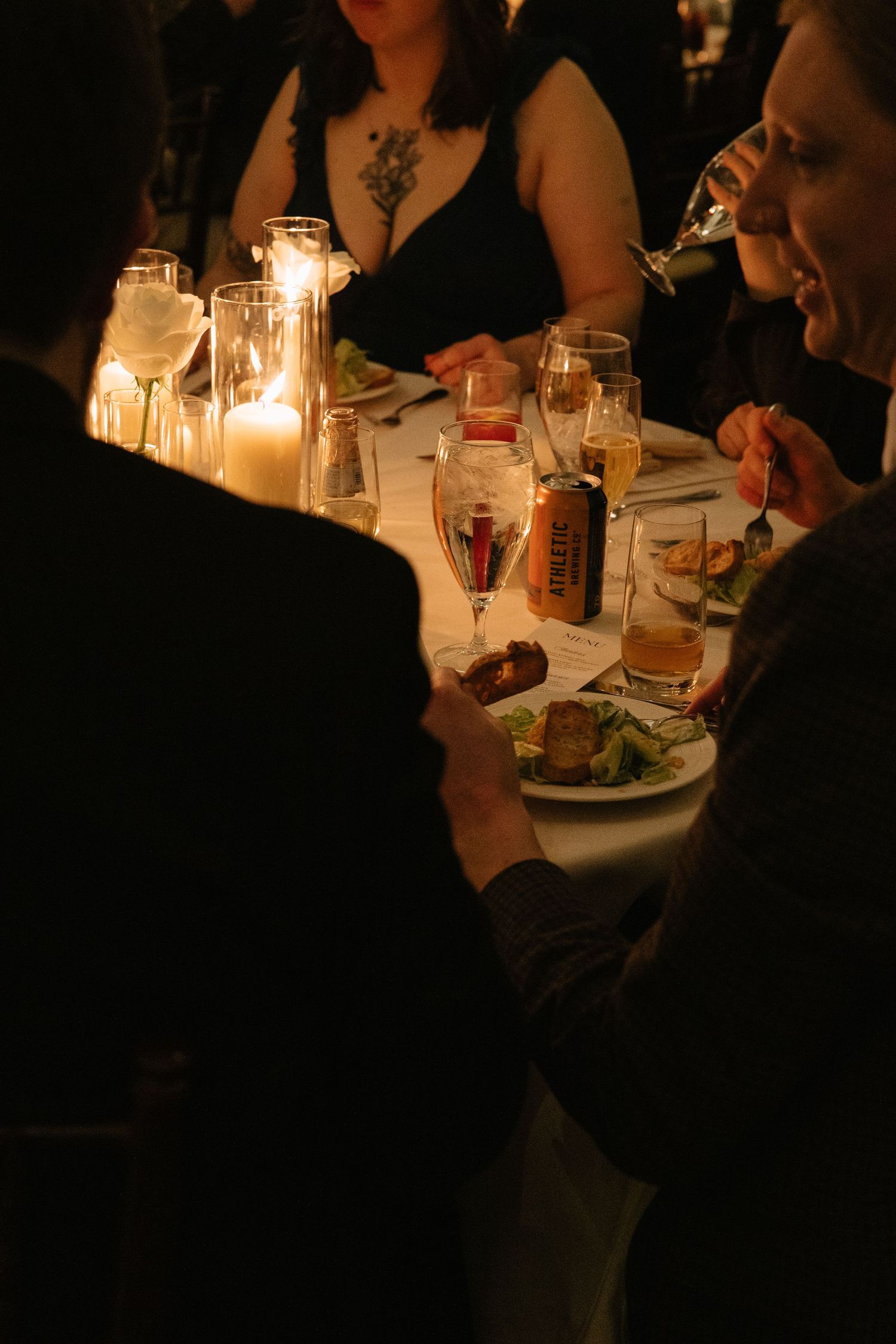 Guests dining by candlelight at an elegant dinner party with champagne flutes and plates of food on a white tablecloth.