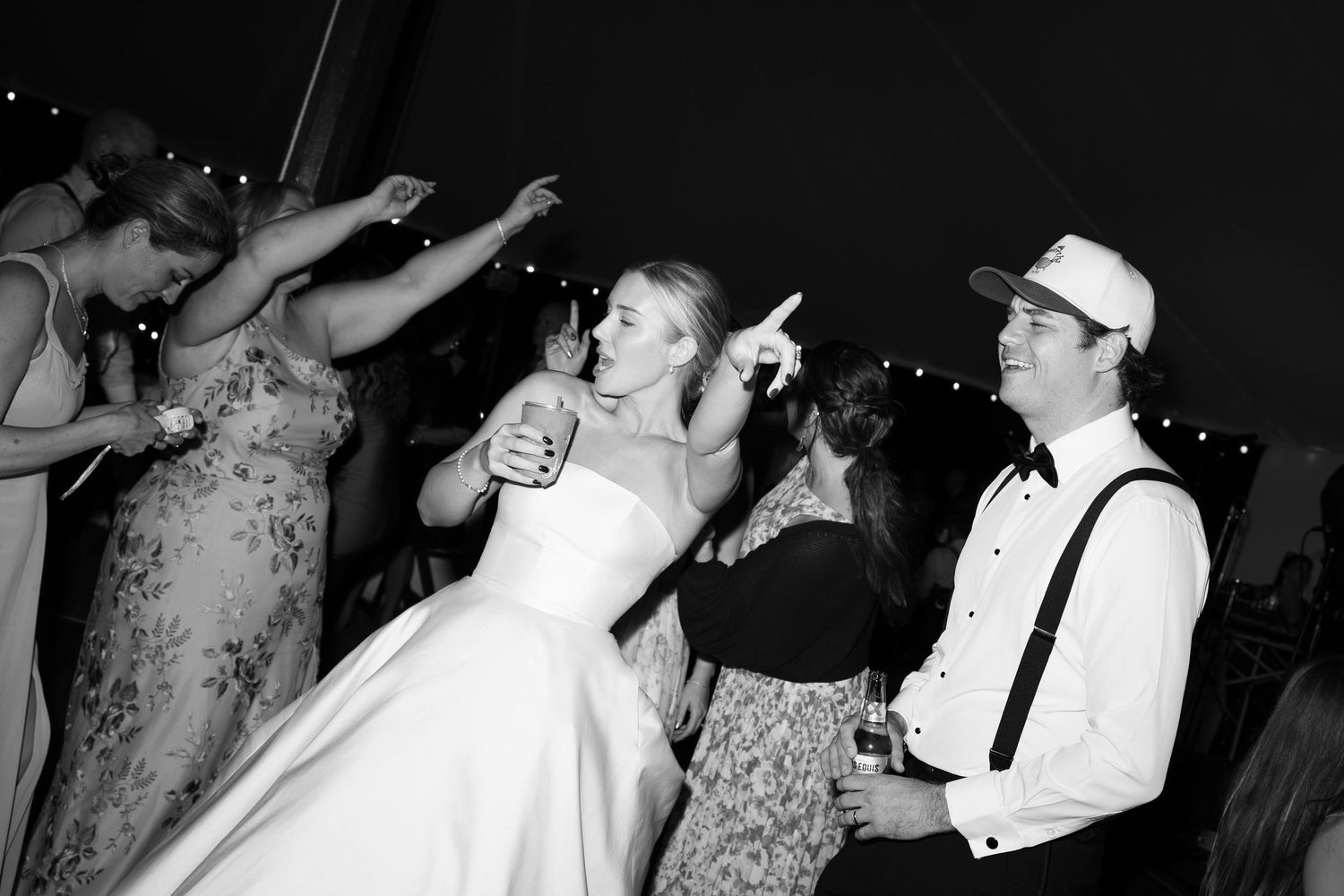Black and white photo of bride dancing joyfully with guests at a lively wedding reception party.