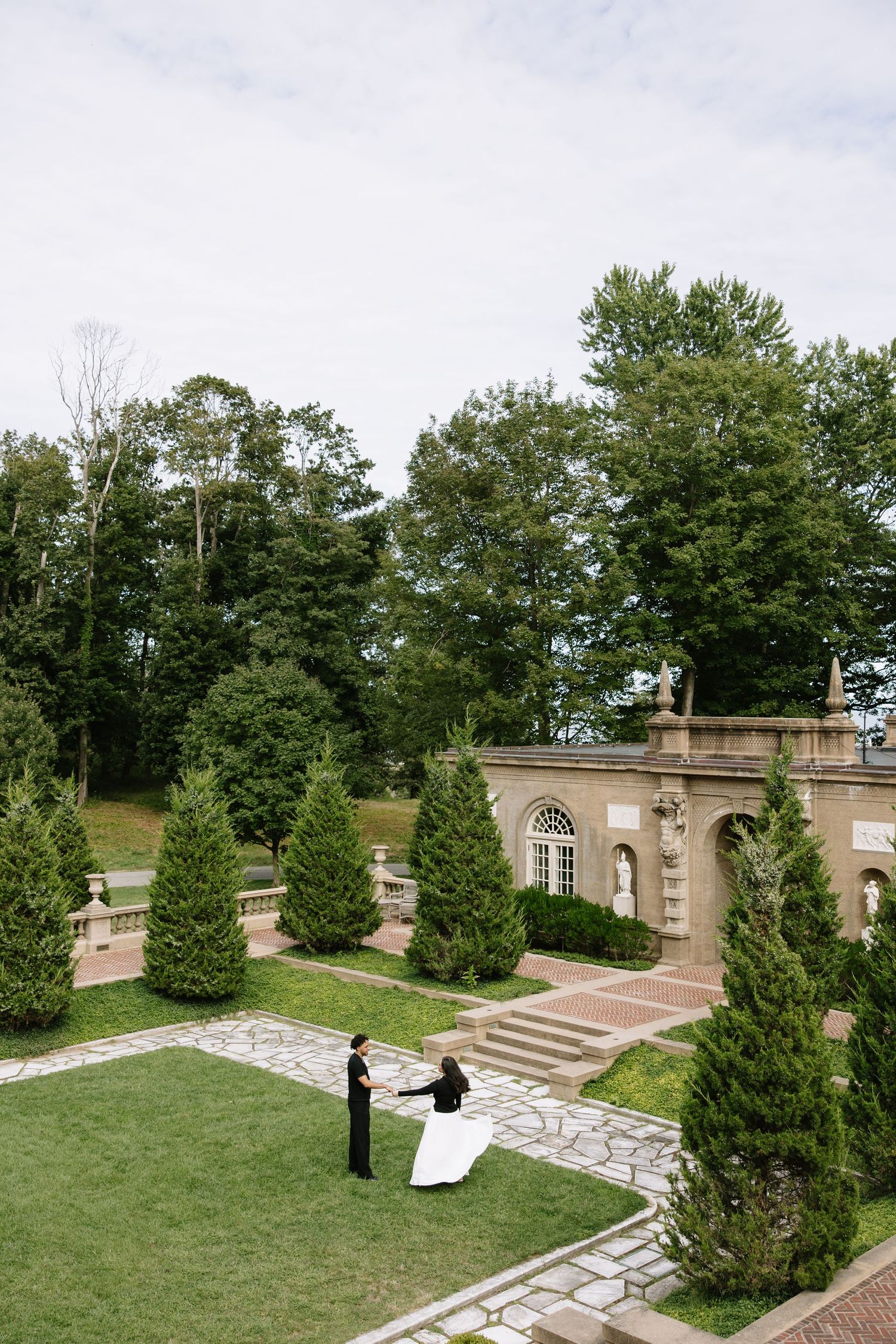 A romantic scene with two people by a stone building surrounded by evergreen trees.