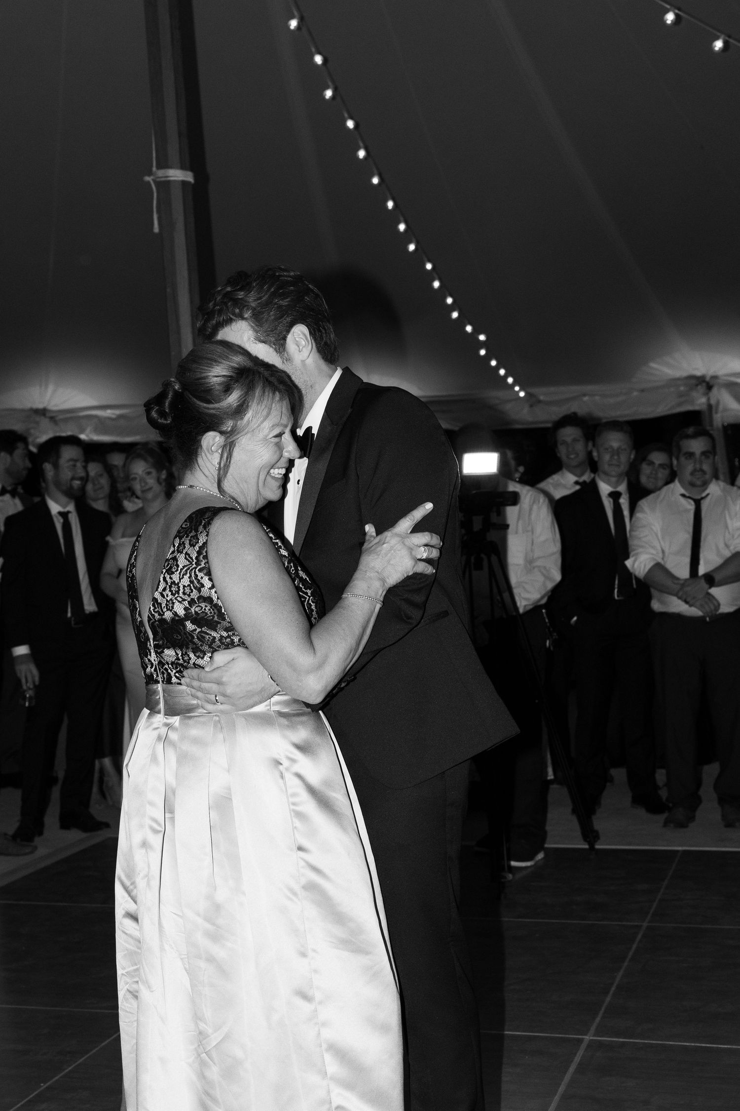 Romantic slow dance at an evening wedding reception with string lights overhead.