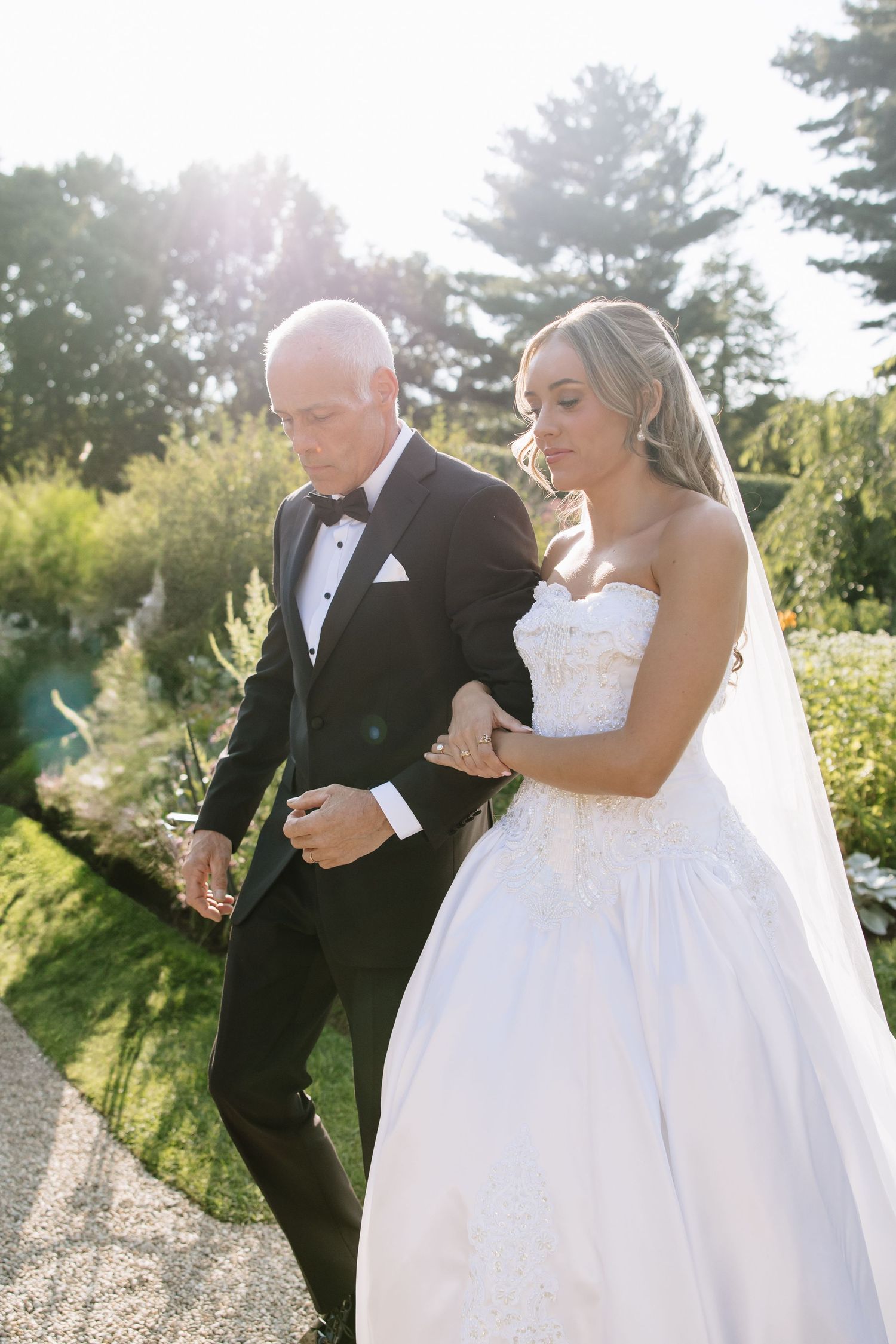 Couple walking and laughing together on a sunny garden path in wedding attire.