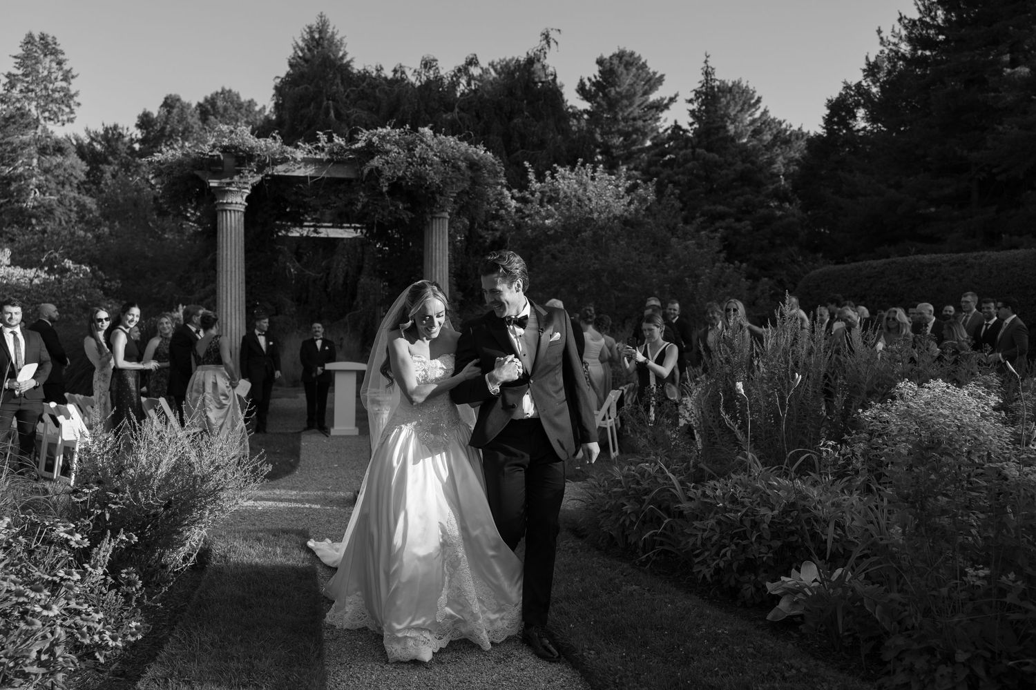 Black and white photo of a wedding ceremony exit through a garden archway.
