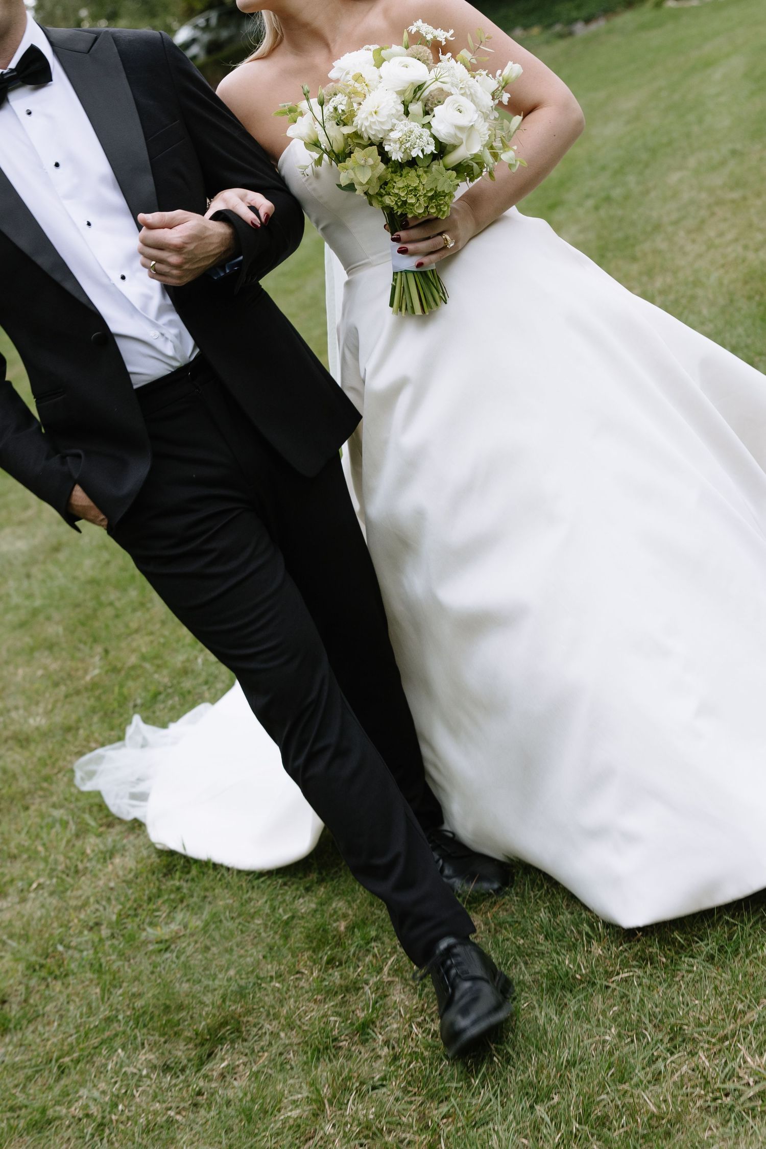 Formal wedding attire and white bouquet captured in detail on green lawn.