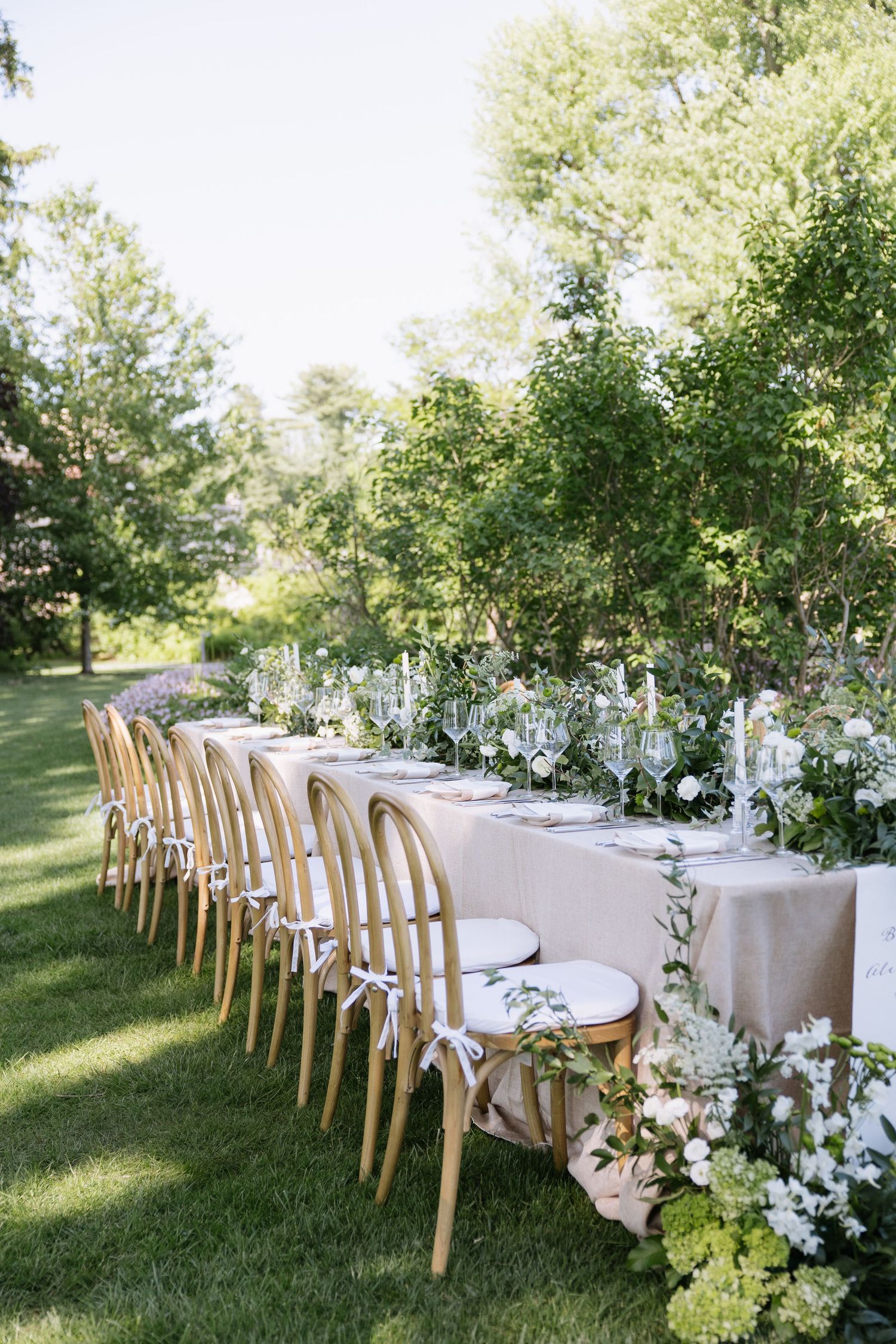 Elegant outdoor wedding reception table with wooden chairs and white floral arrangements.