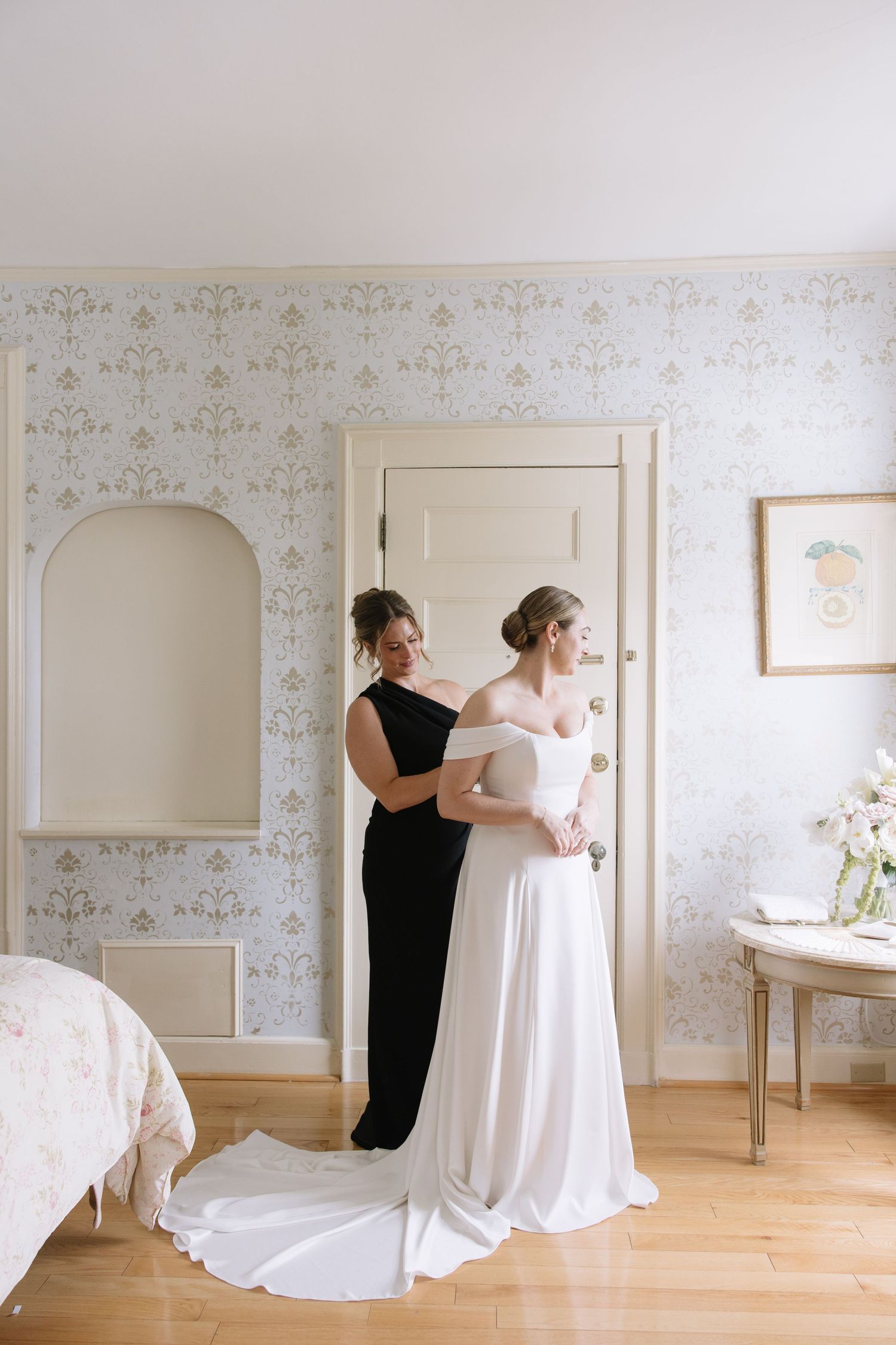 Getting ready scene in elegant wallpapered room with wedding dress preparation.