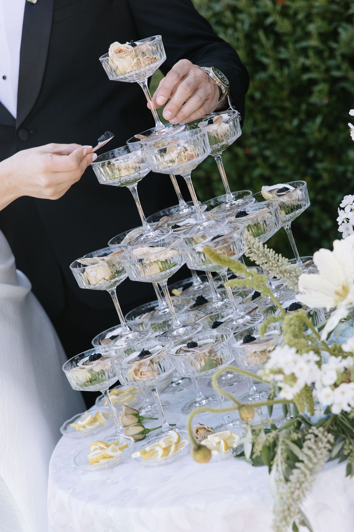 Elegant champagne tower with coupe glasses arranged in pyramid shape at a wedding reception, adorned with floral decorations.