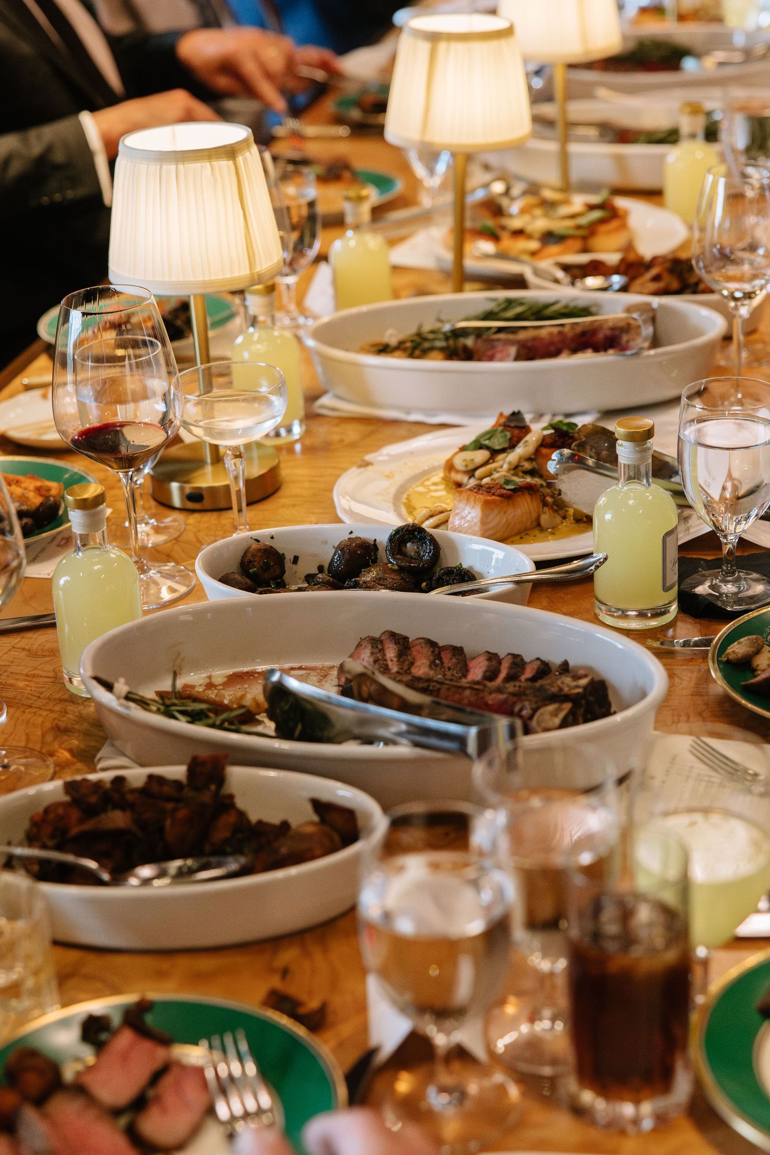 Elegant dinner table spread with grilled meats, roasted vegetables, wine glasses, and glowing lamps at a upscale restaurant.