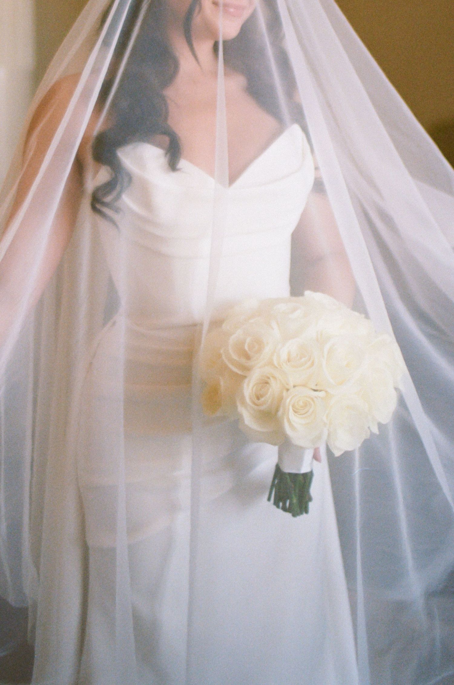 Ethereal bridal portrait with white roses bouquet and flowing veil in soft focus.