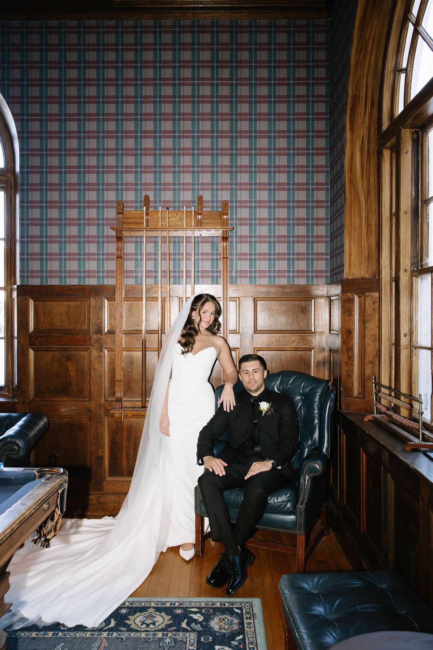 Wedding portraits taken in a vintage room with plaid wallpaper and leather furniture.