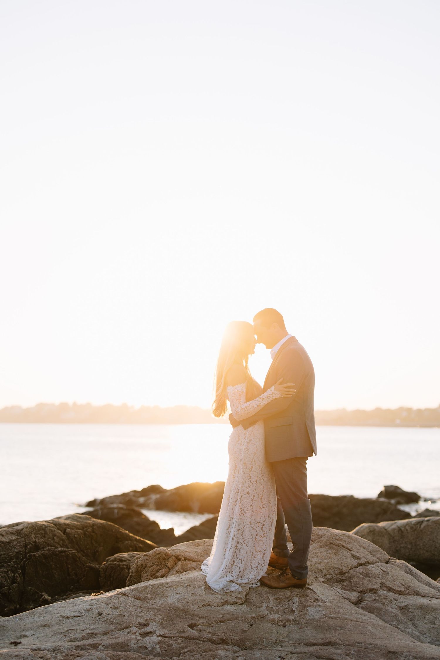 Intimate moment between couple on coastal rocks during golden hour.