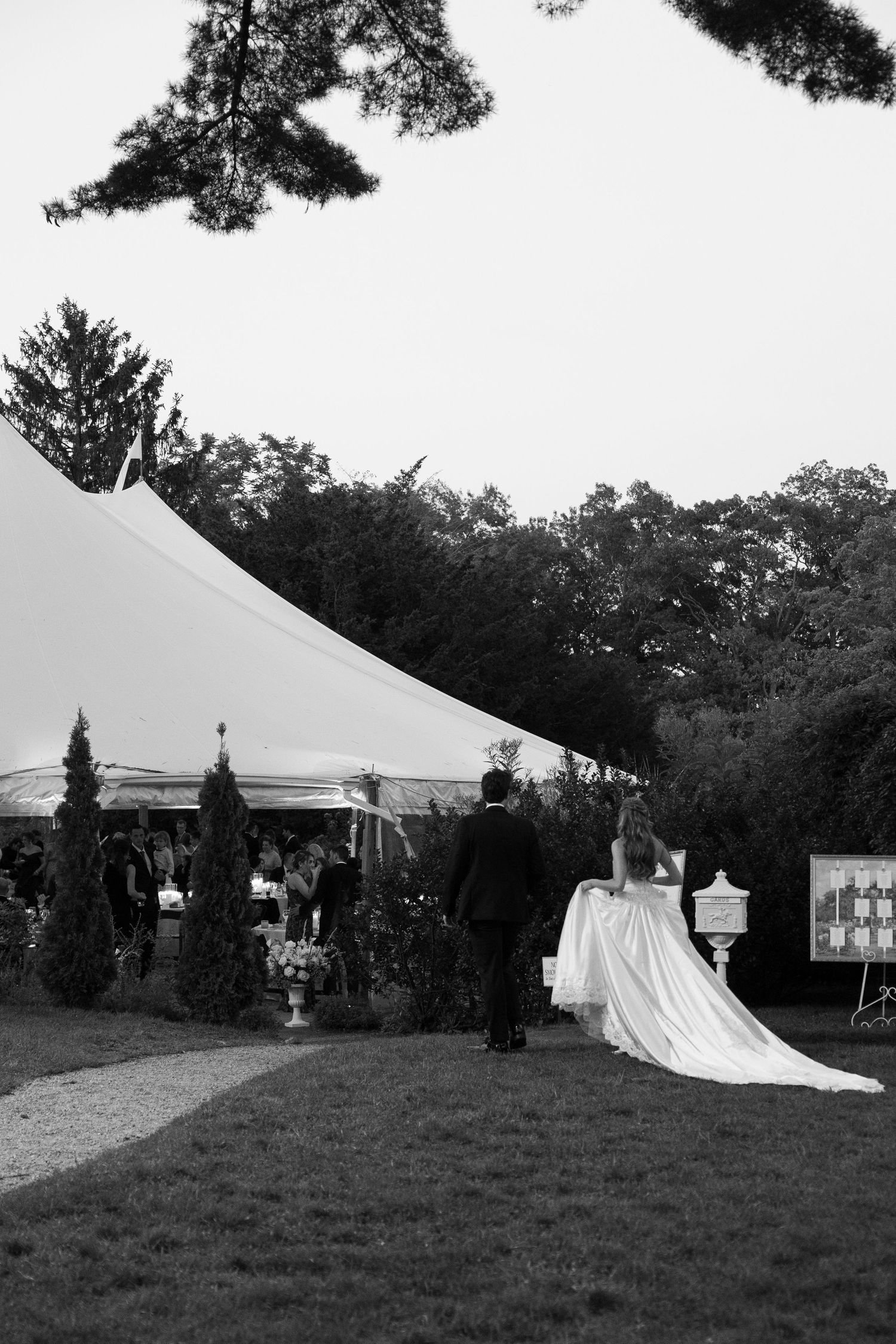 Large white wedding tent set up on a grassy hill with trees in the background.