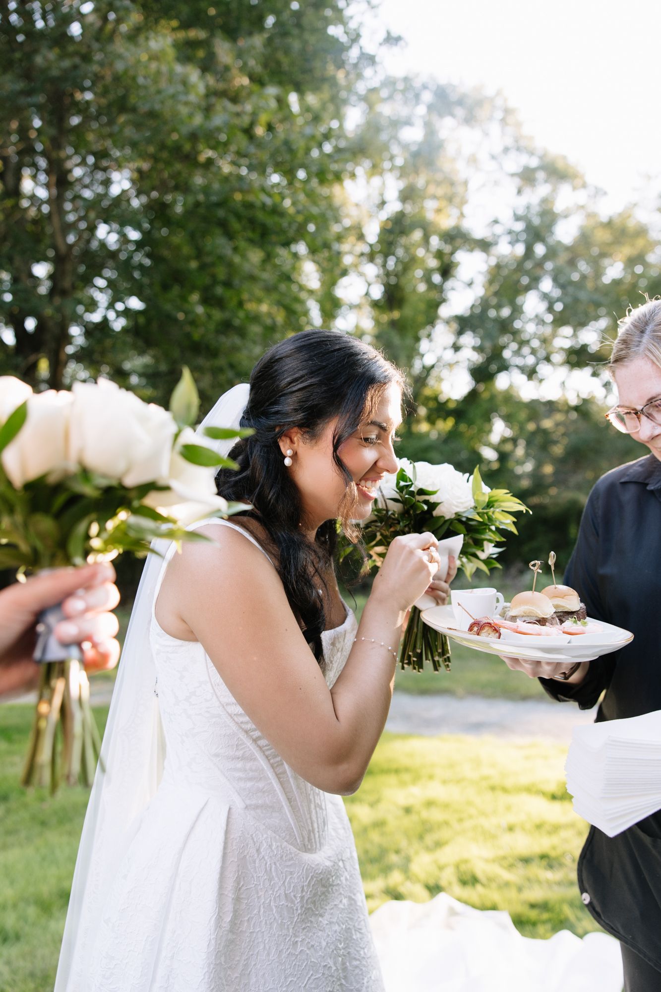 Bride in white dress enjoying wedding cake at an outdoor reception.