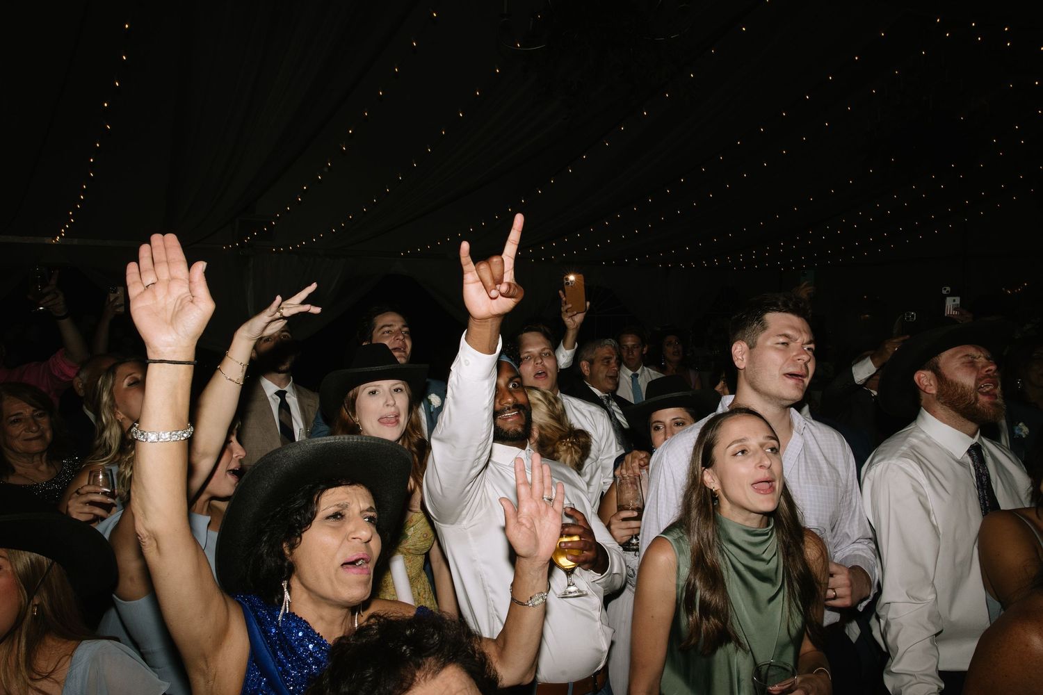 Wedding guests dancing and celebrating enthusiastically on a dark dance floor.