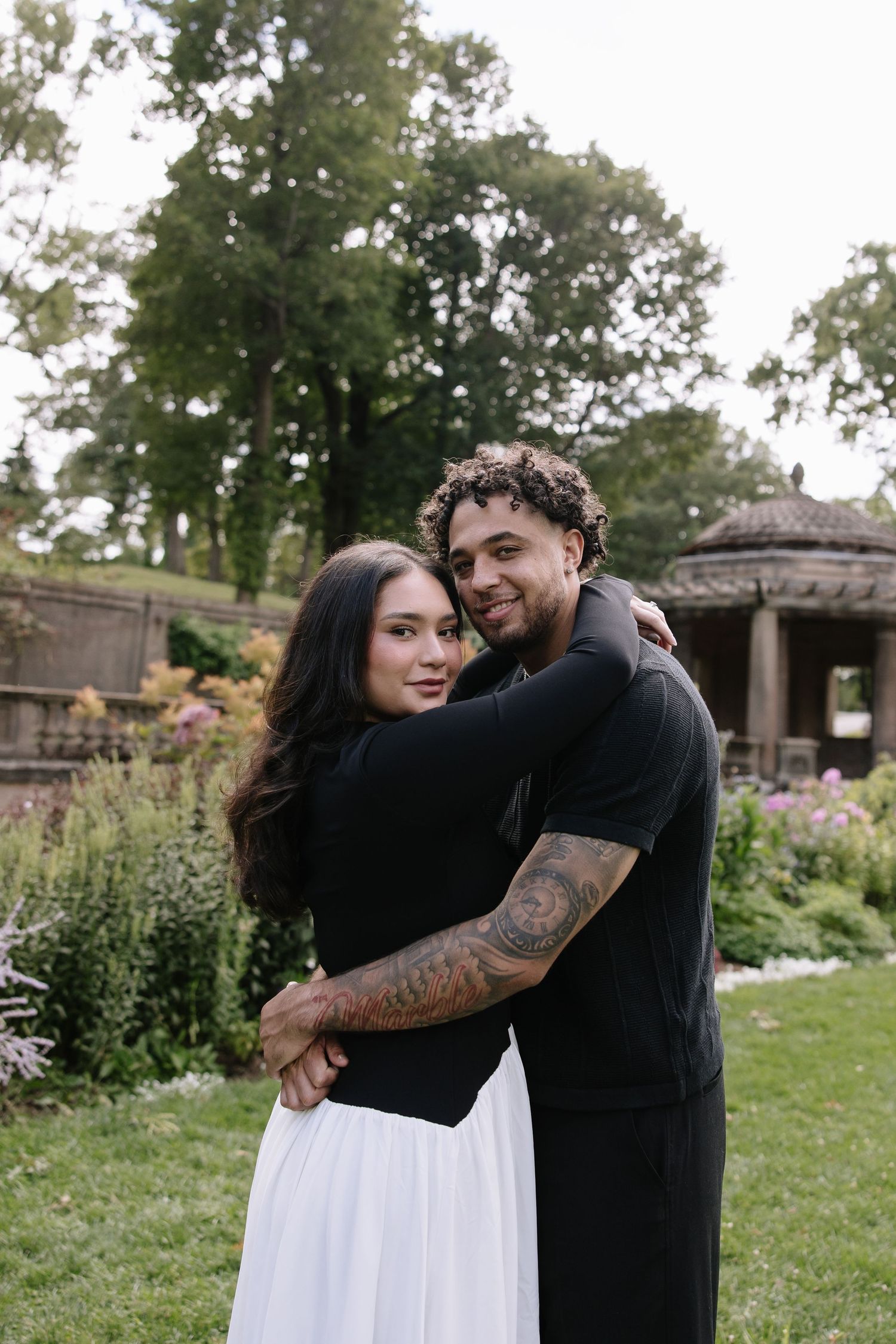 A tender embrace captured in an outdoor garden setting with natural greenery.