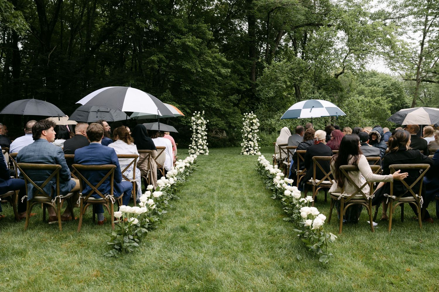 Outdoor wedding ceremony setup with rows of chairs and umbrellas on a green lawn.