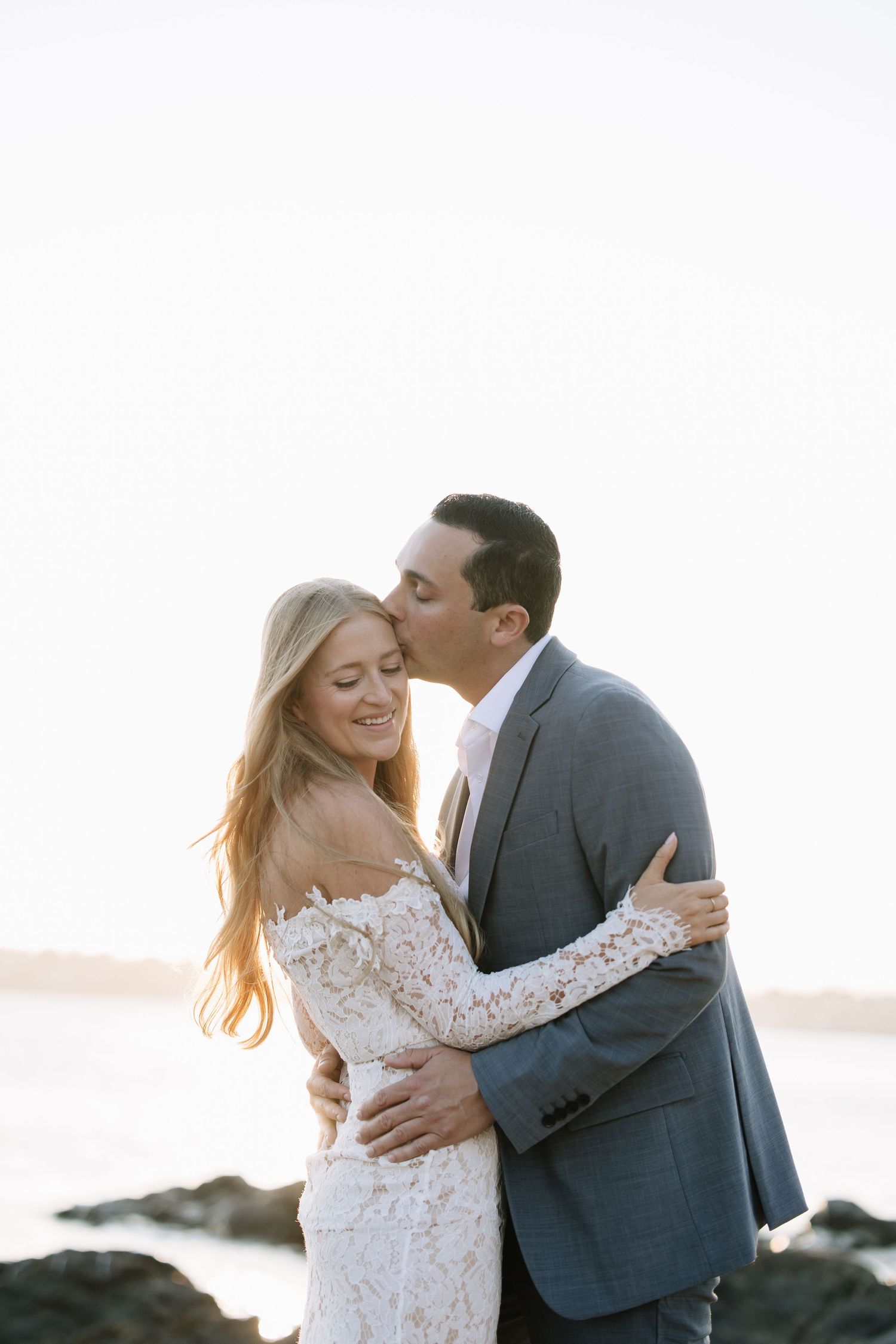 Romantic moment captured between couple on rocky beach at sunset.