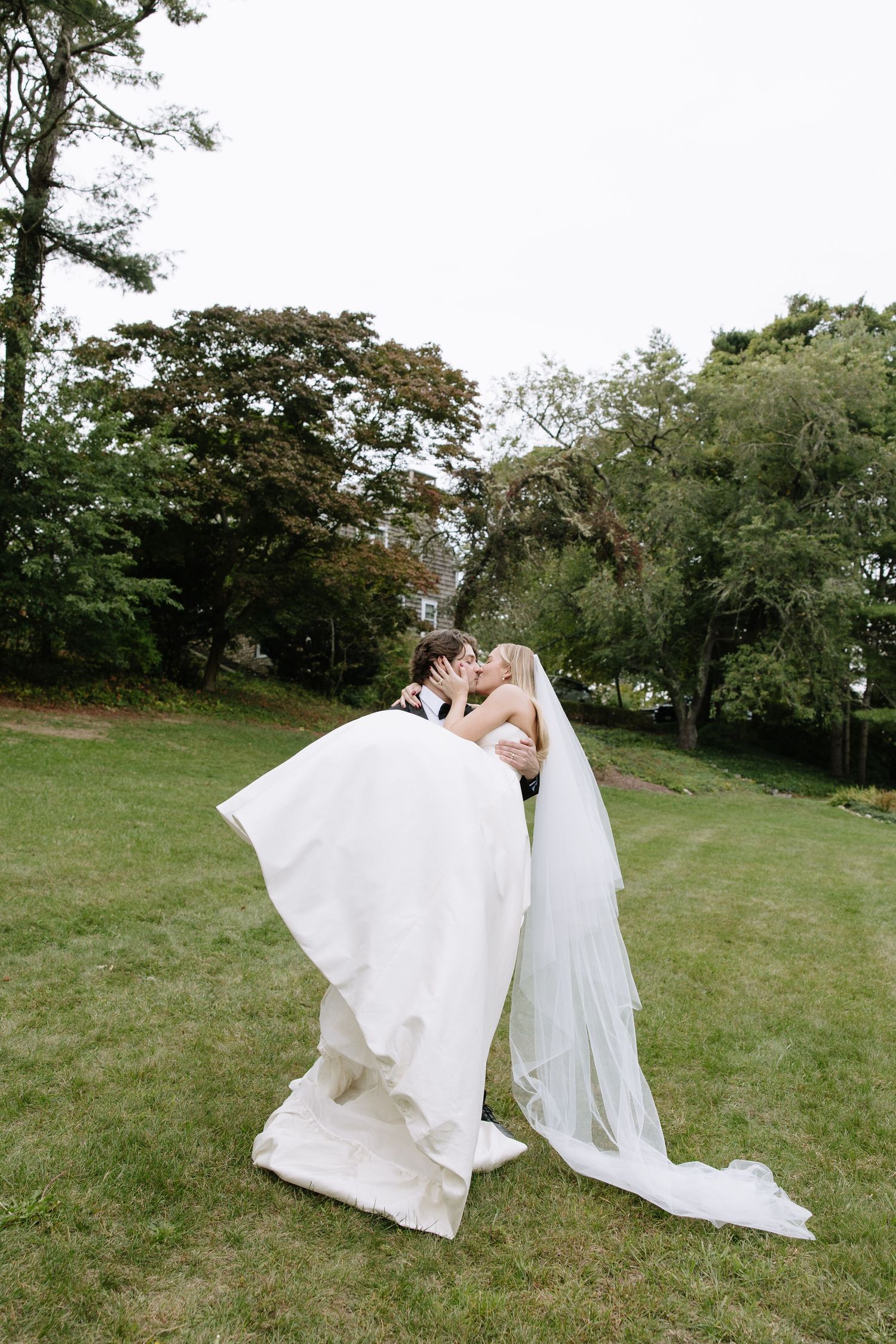 A wedding couple walking through a grassy field with flowing white dress and veil in the breeze.