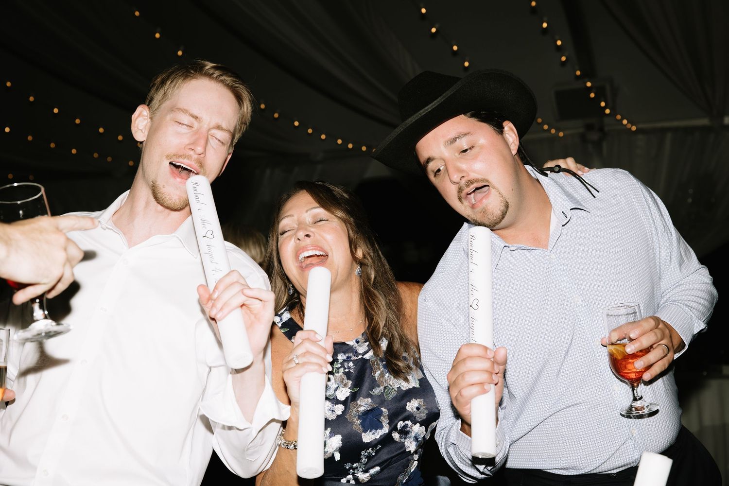 Party guests laughing while holding glow sticks at nighttime celebration.
