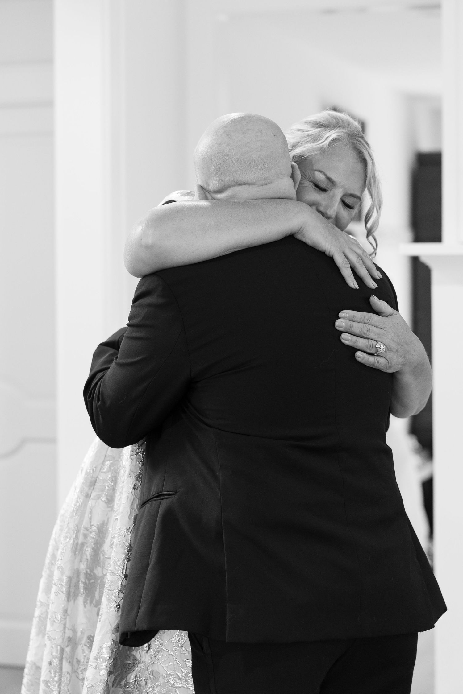 Black and white photo of bride and groom sharing an emotional hug during wedding celebration.