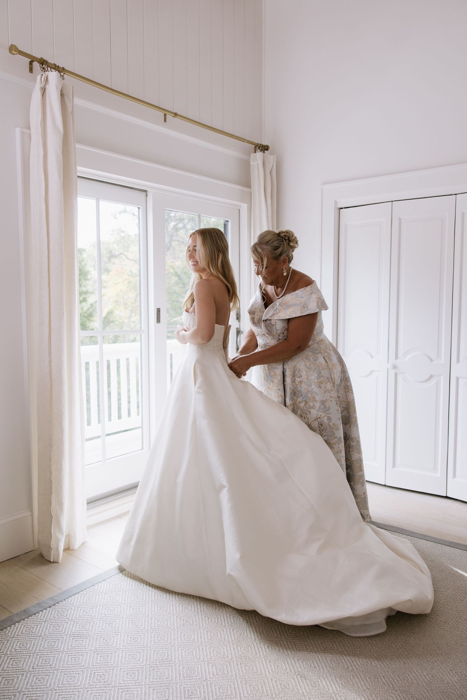 Wedding dress preparation in bright white room with natural light streaming through windows.