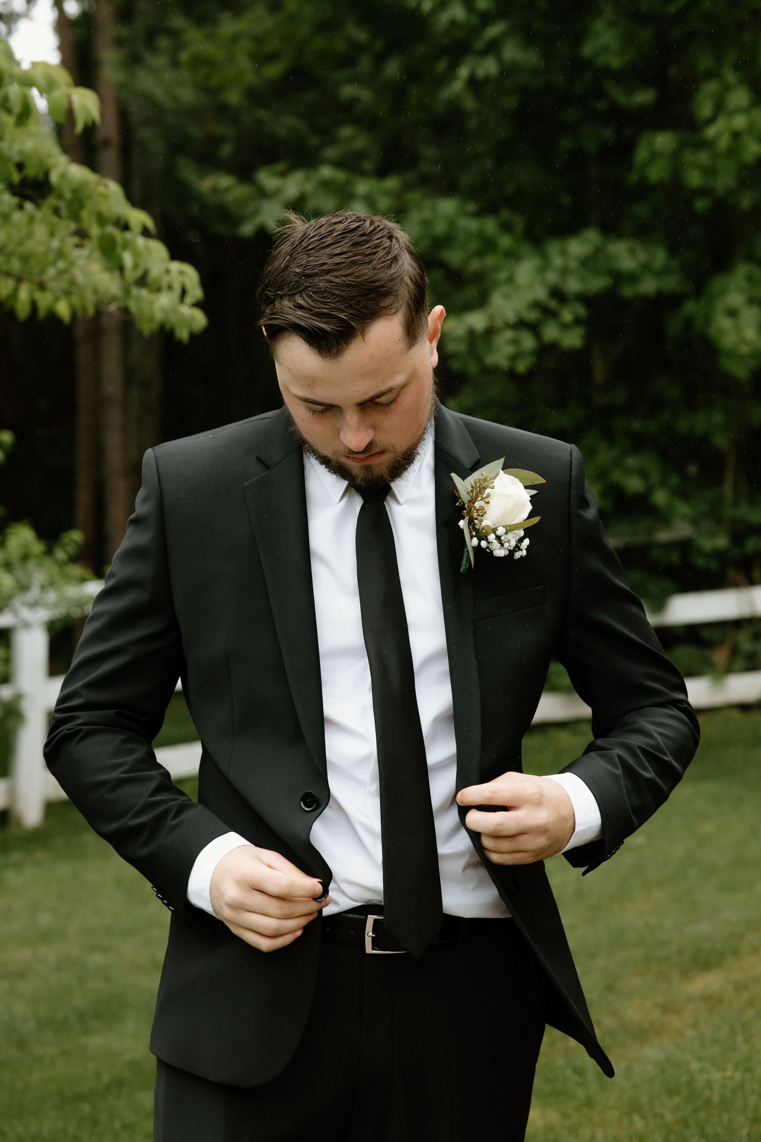 Groom in formal black suit adjusts his tie before the ceremony.