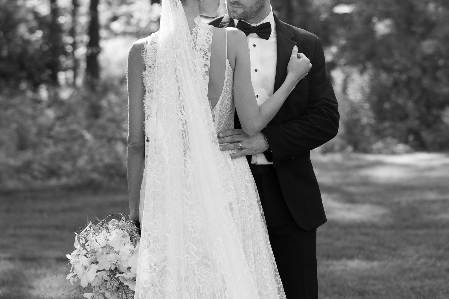 A romantic wedding portrait showing a flowing white dress and black tuxedo in an outdoor setting.