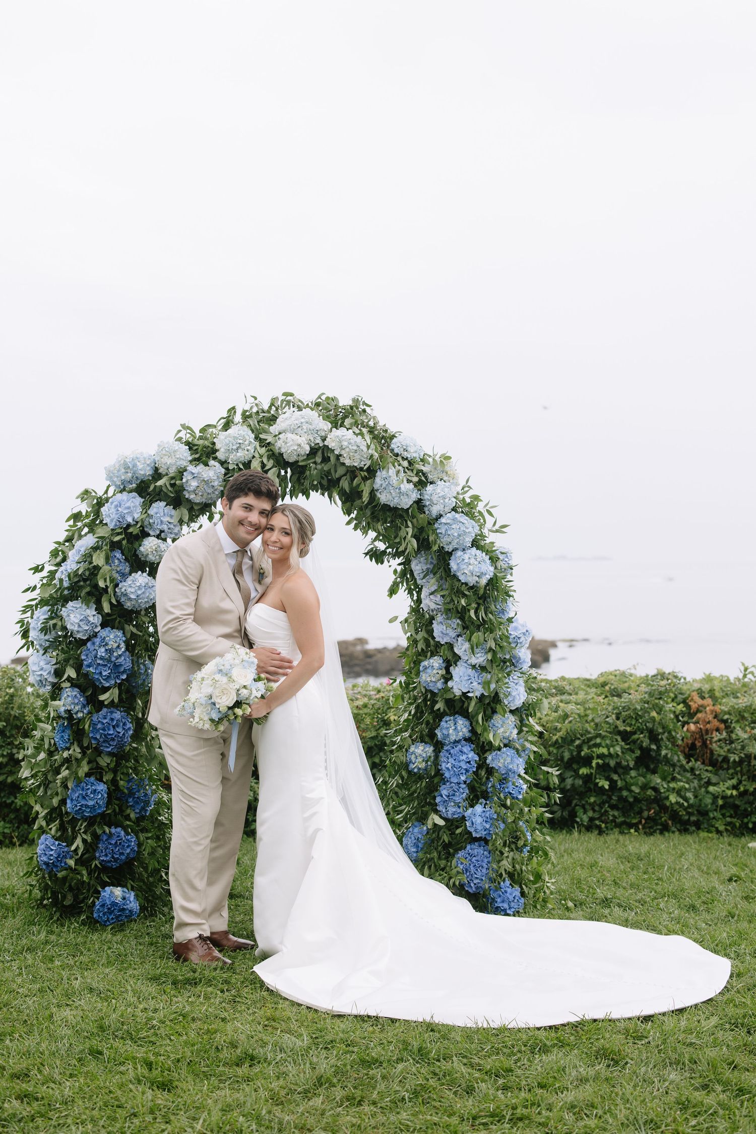Wedding ceremony setup with blue hydrangea floral arch overlooking the ocean.