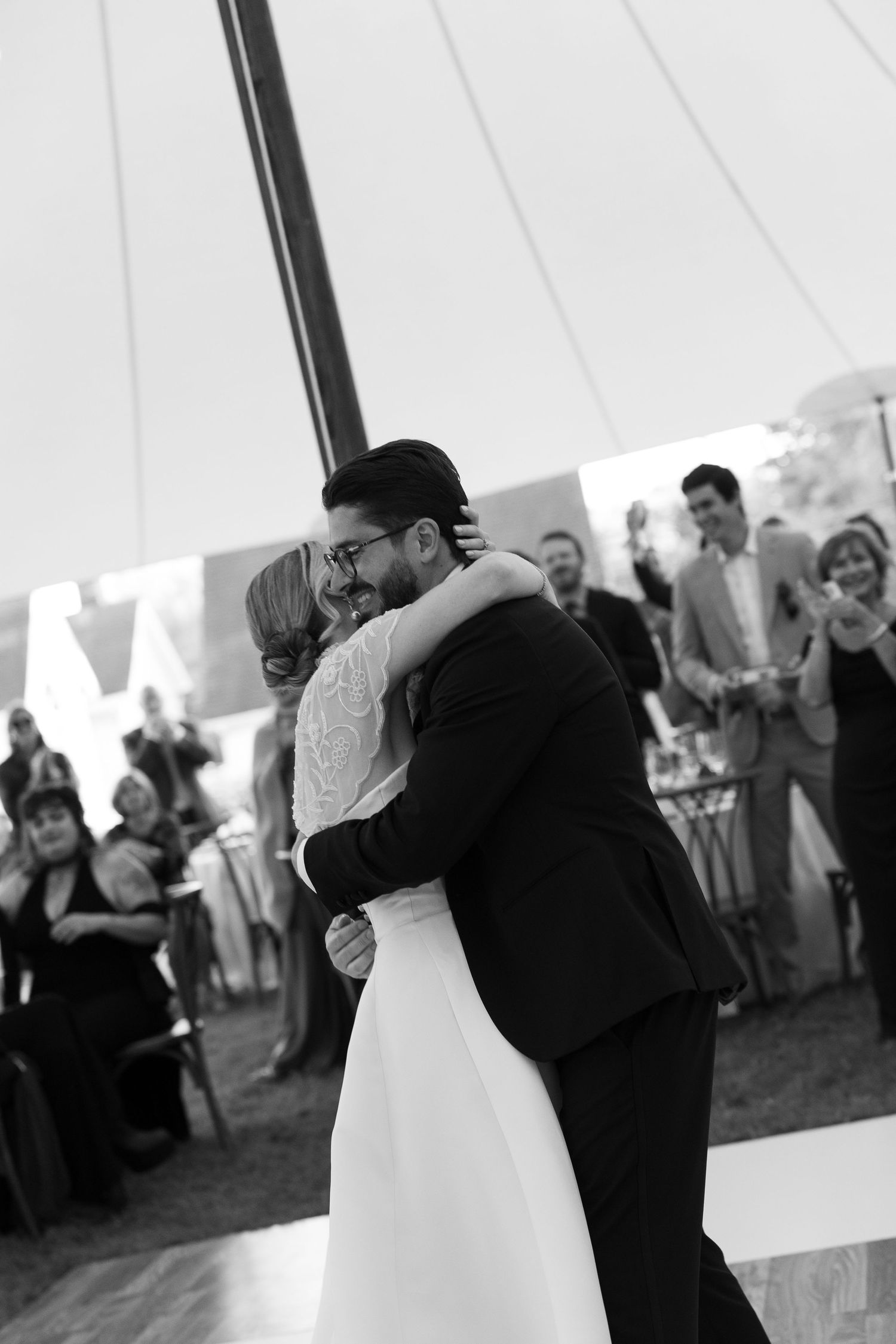 Black and white photo of bride and groom sharing their first dance under a tent at their wedding reception.