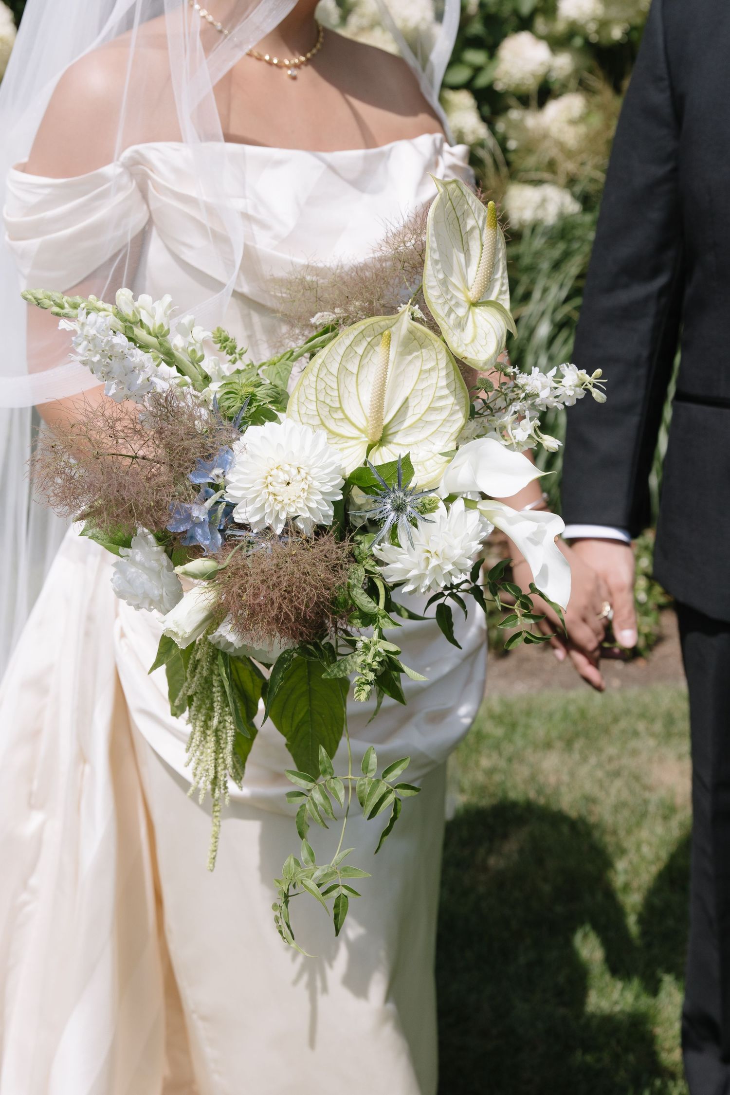 Bride holding a lush white wedding bouquet with anthuriums, dahlias, and greenery in an elegant satin gown.