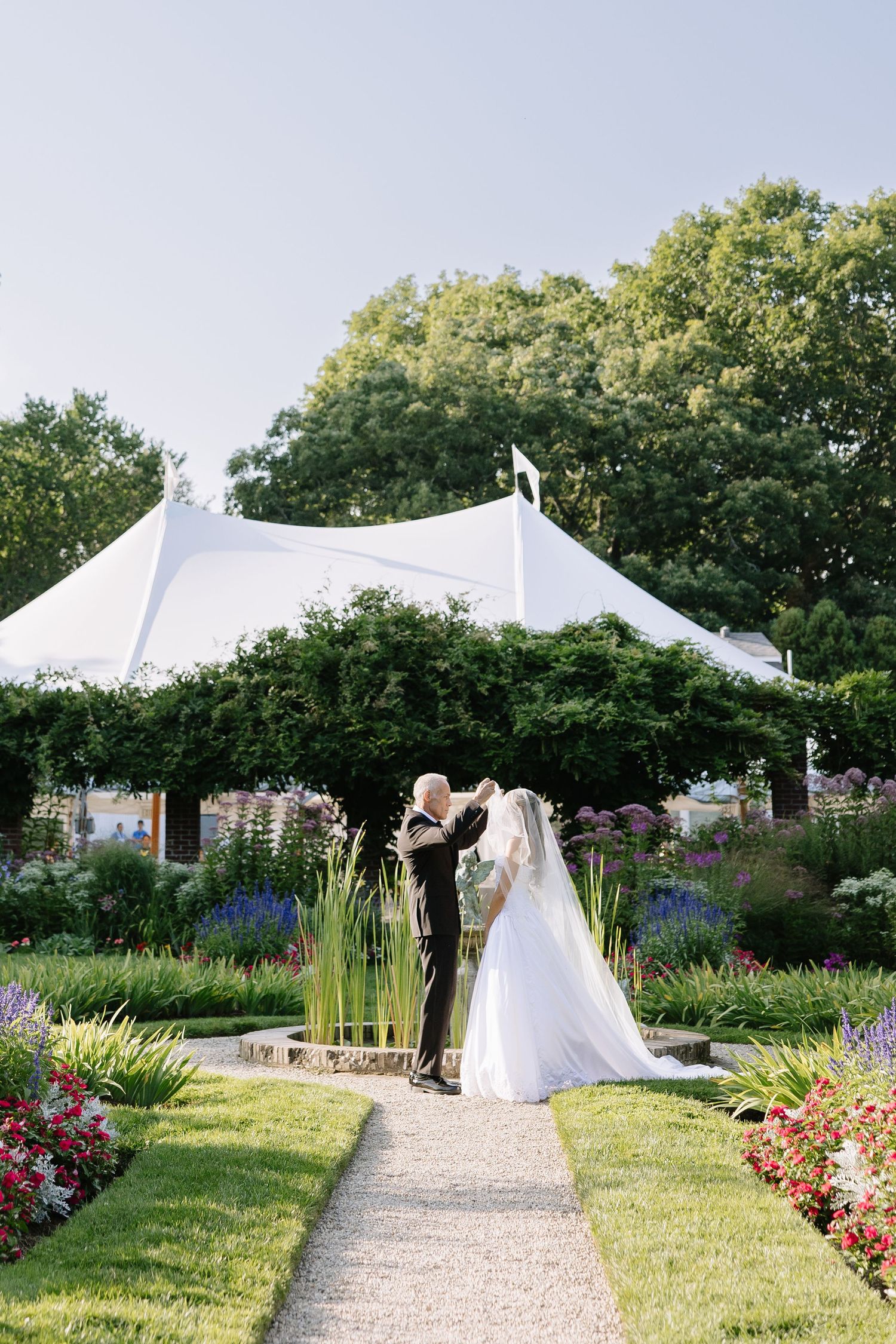 Elegant garden wedding ceremony setup with white tent and floral arrangements along a stone path.
