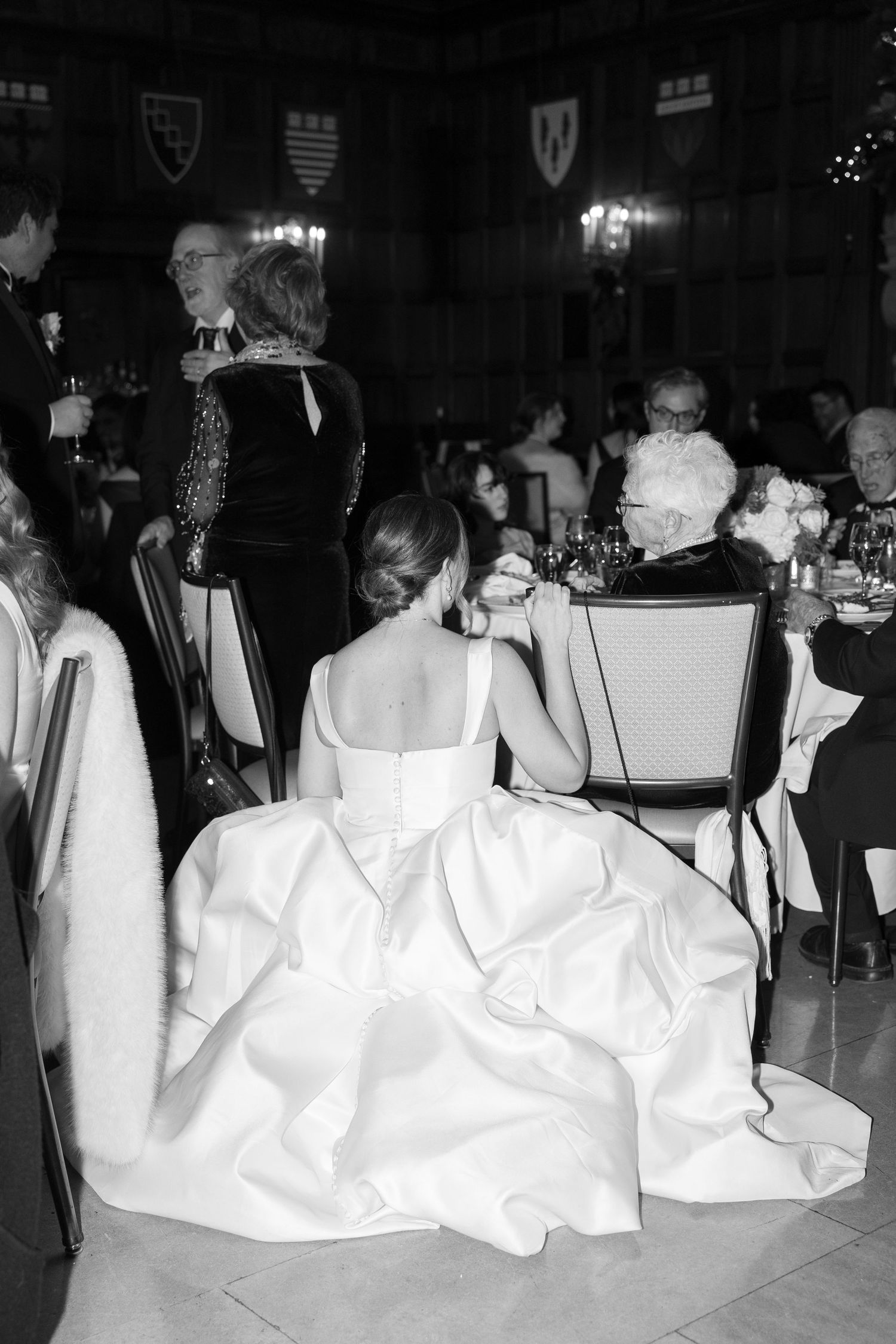Wedding guests seated at reception tables with flowing white dresses visible.