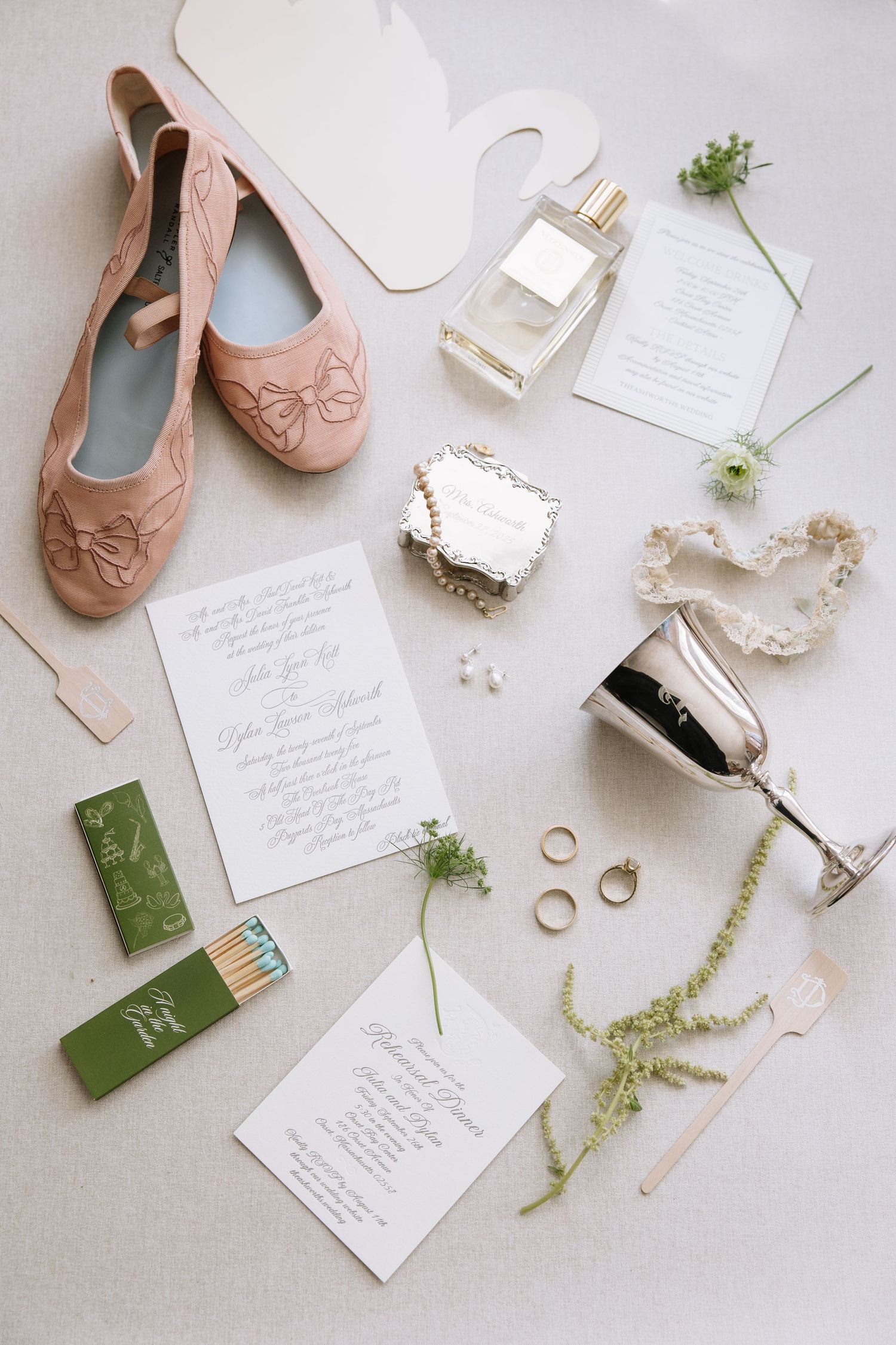 Flat lay of wedding details including pink ballet flats, invitations, rings and greenery.