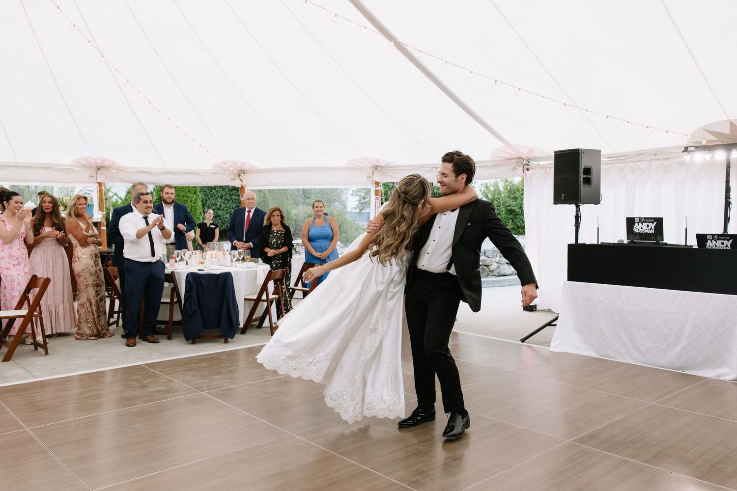 Wedding guests dance and celebrate on an outdoor dance floor under a white tent.