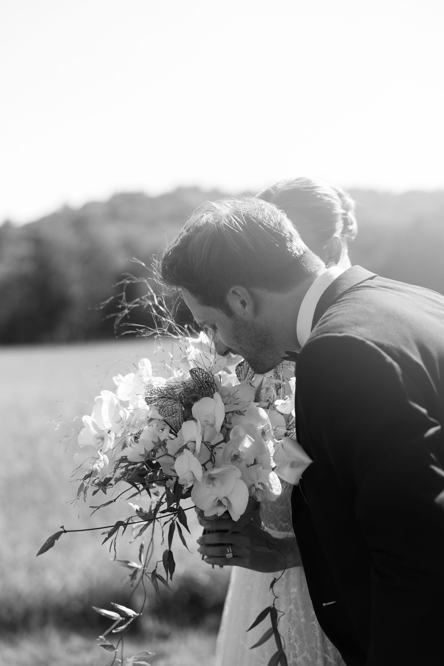 Bride and groom sharing a romantic moment smelling a beautiful white wedding bouquet.