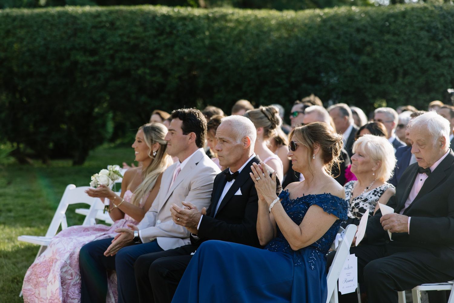 Guests seated outdoors at an elegant wedding ceremony, dressed in formal attire, enjoying the celebration.