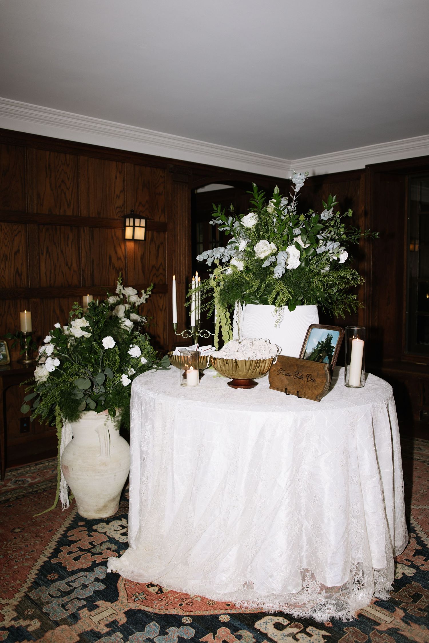 Wedding reception tables with white linens, floral arrangements and candles against dark wood-paneled walls.