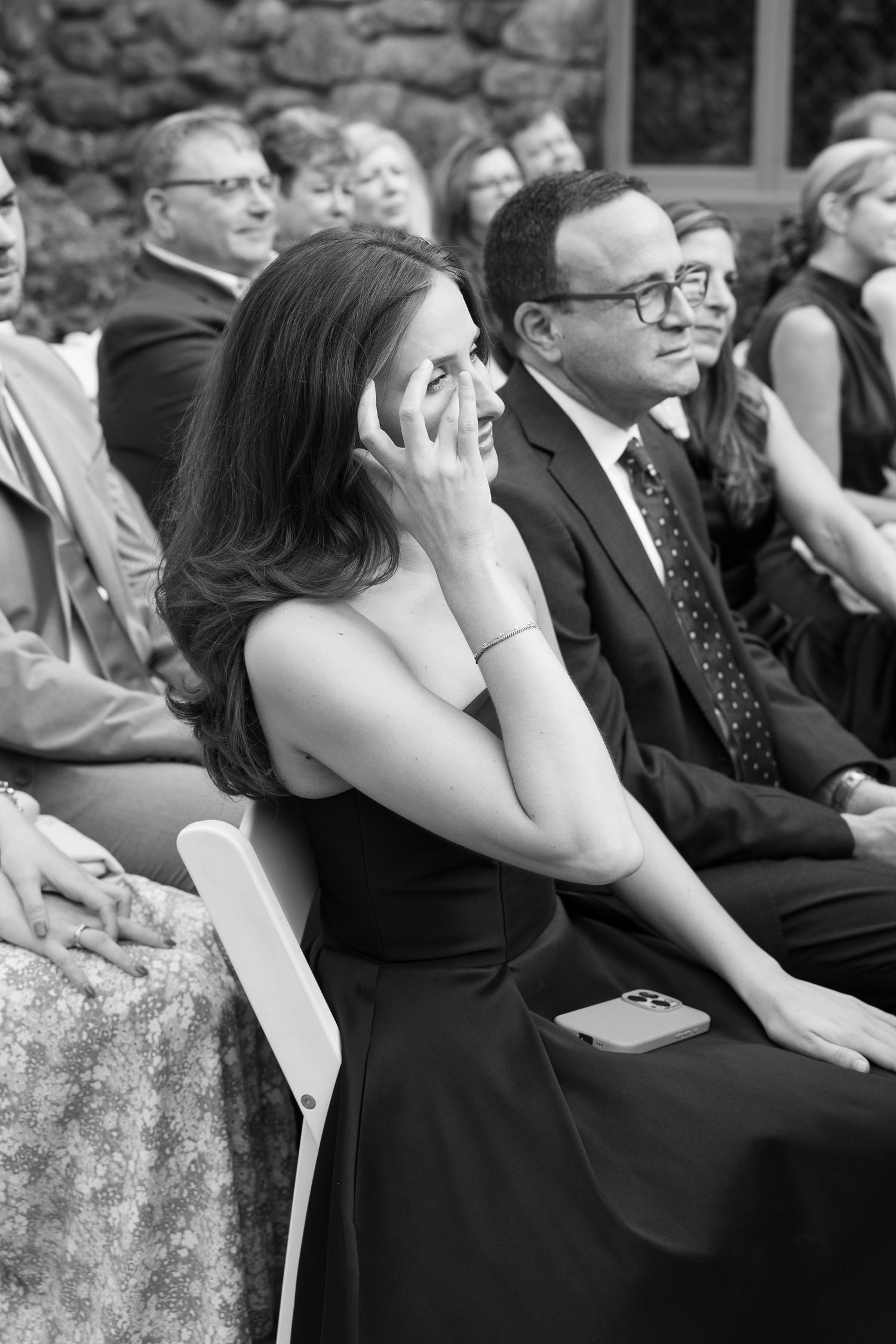 Emotional wedding guest wiping tears during outdoor ceremony in black and white photo.