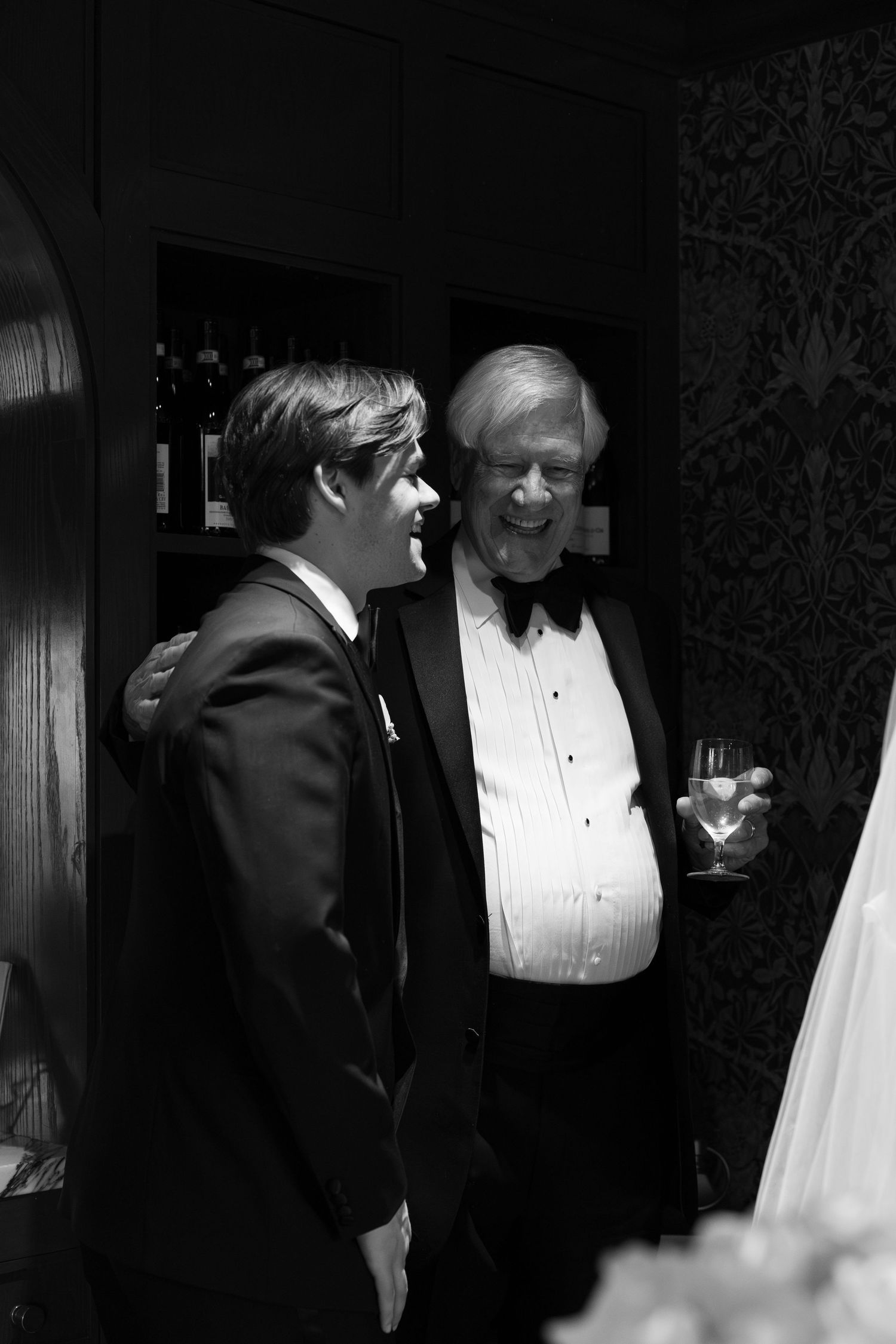 Black and white photo of two men in tuxedos smiling at a formal wedding reception event.