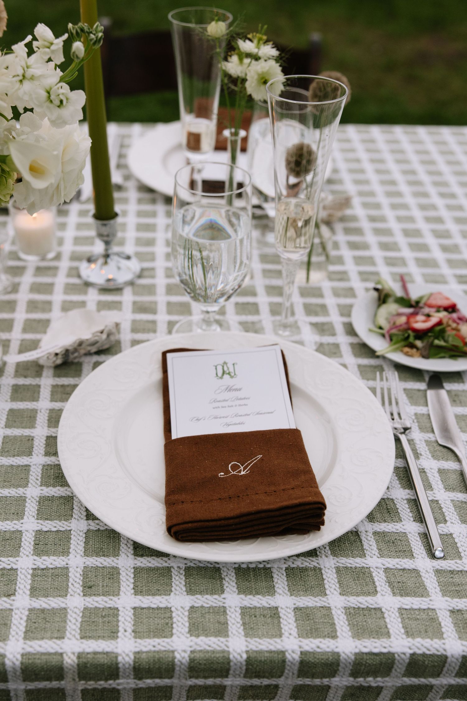Elegant table setting with checkered tablecloth, white plates, and wooden menu holders.