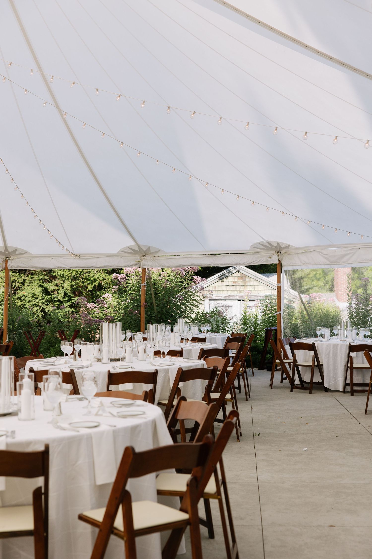 An elegant wedding reception tent with white tablecloths and wooden chairs set for dining.