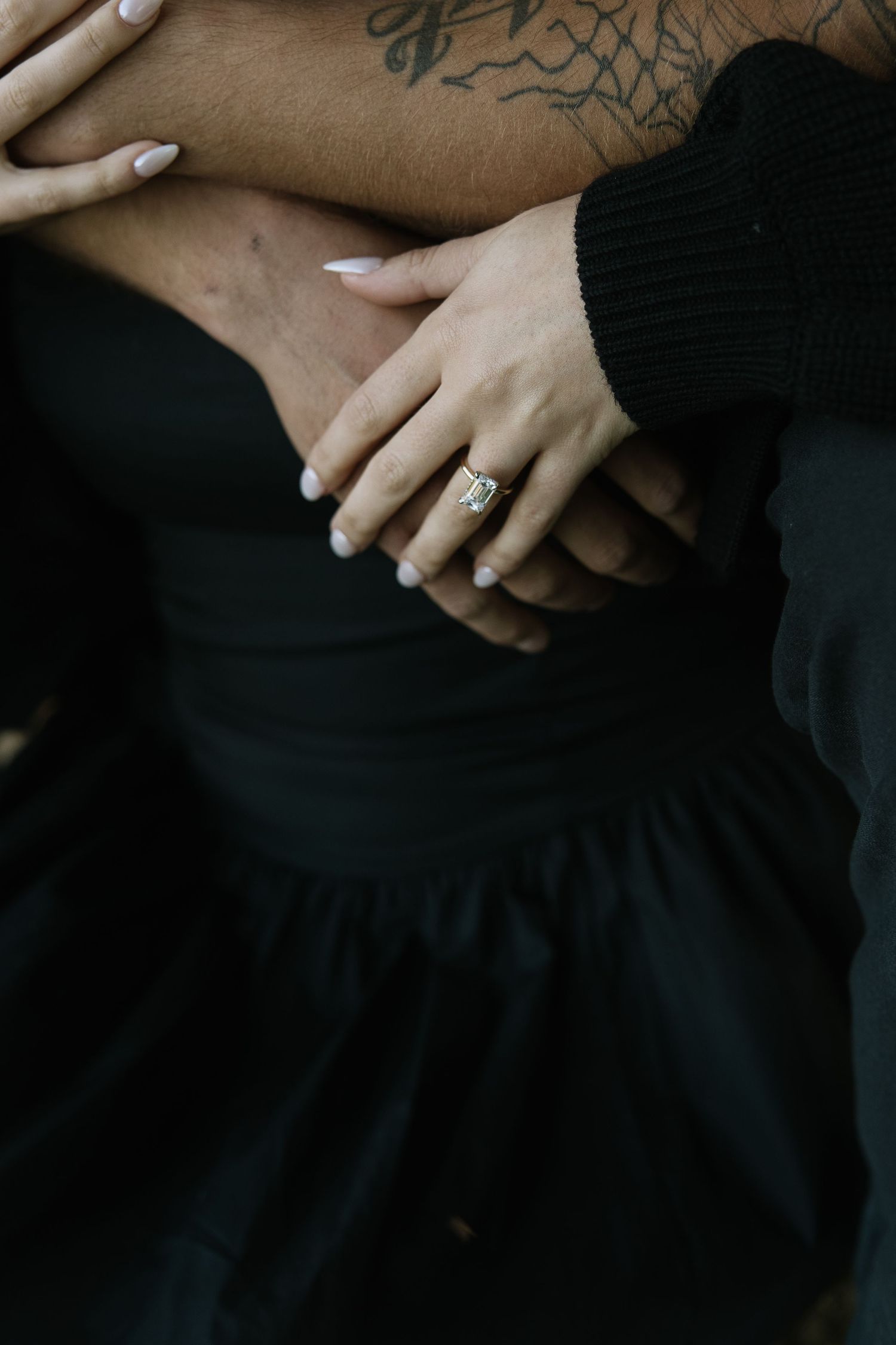 Close-up of hands resting on black fabric, showing intimate connection and detail.