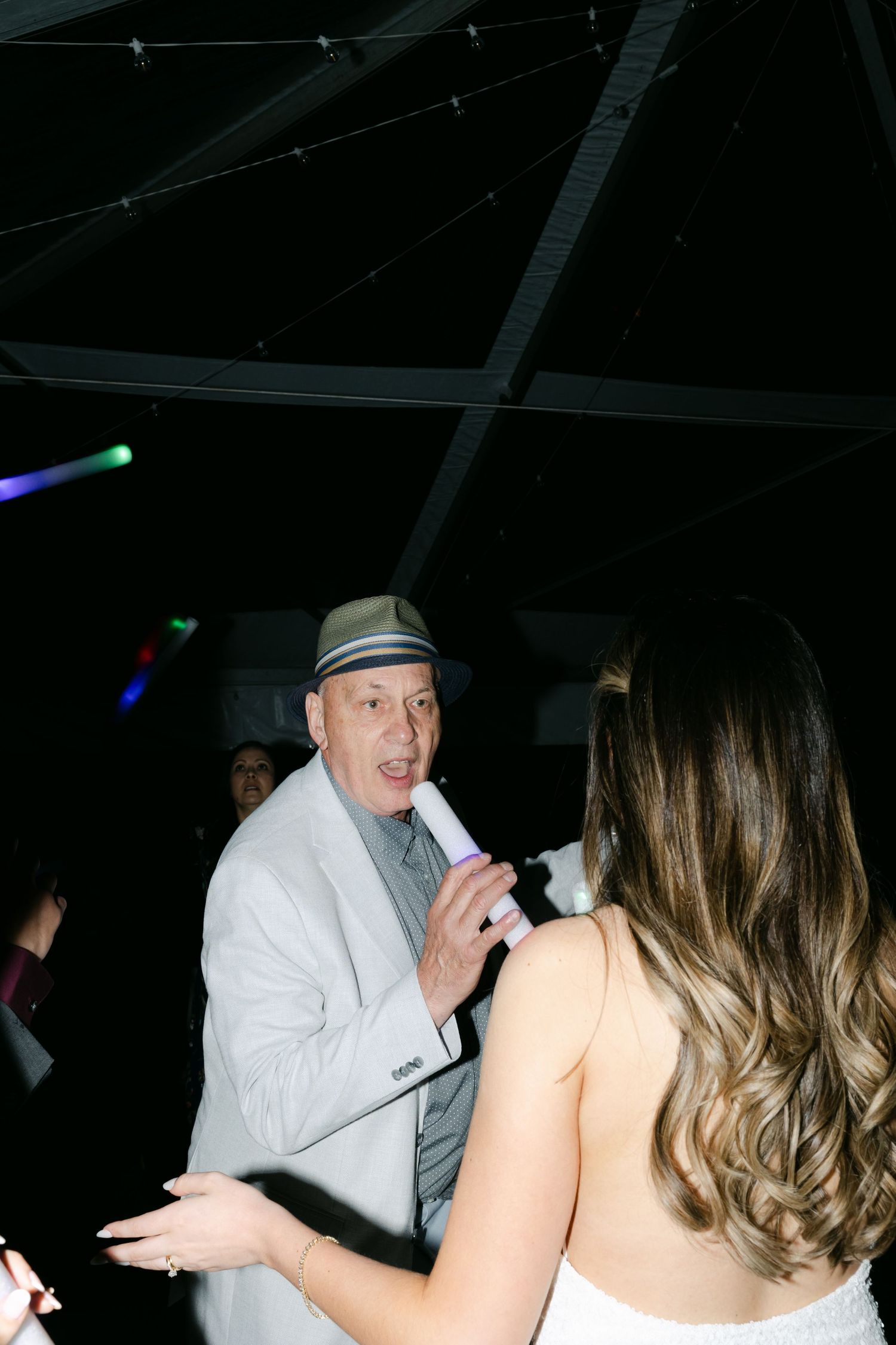 Wedding reception party scene with guests dancing and celebrating in dim lighting.