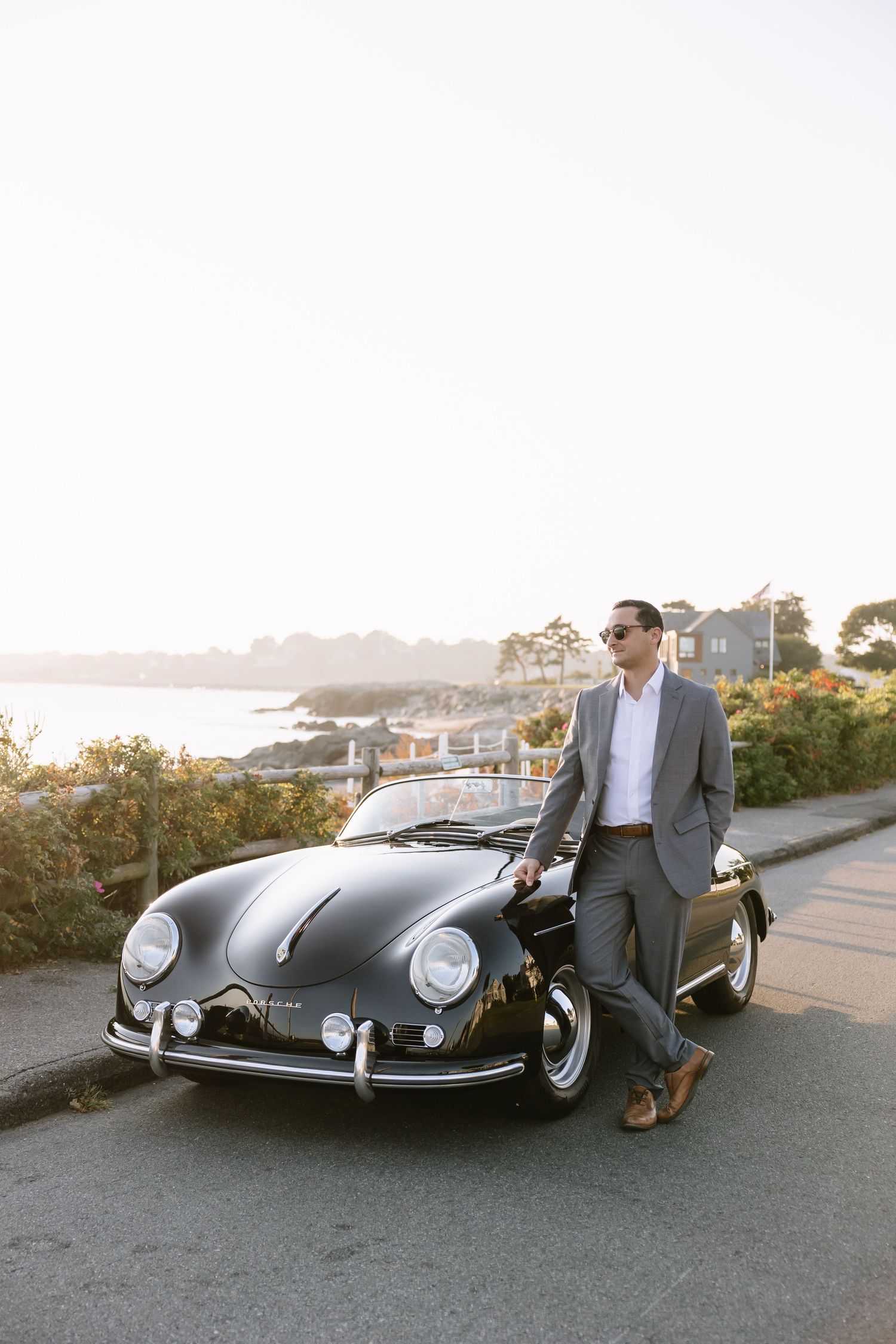 Classic black Porsche 356 convertible parked on coastal road at sunset.
