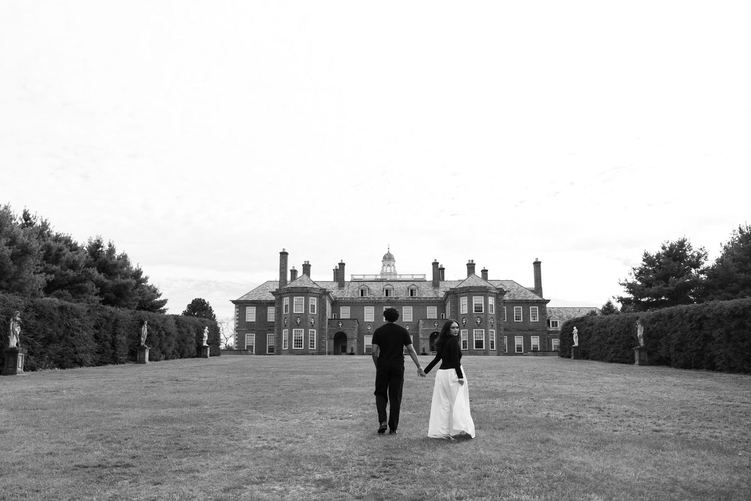 A distant view of a stately mansion across expansive grounds in black and white photography.