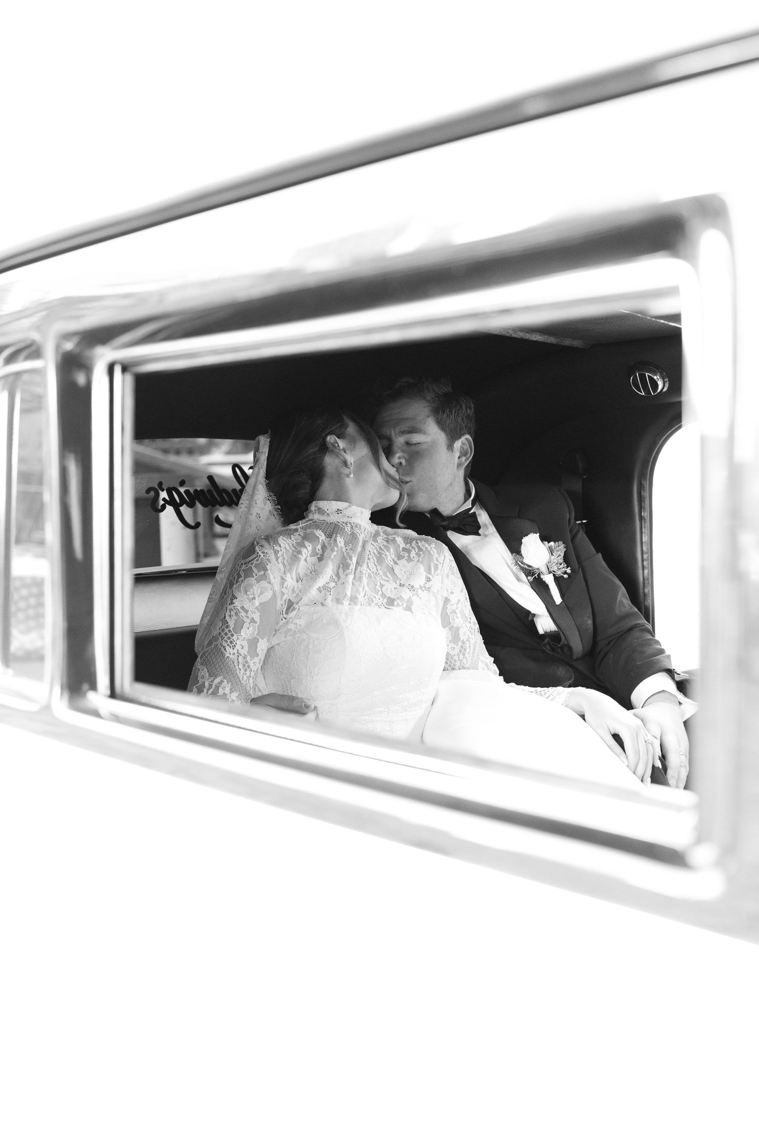 Wedding party members look out car windows in a classic black and white photograph.