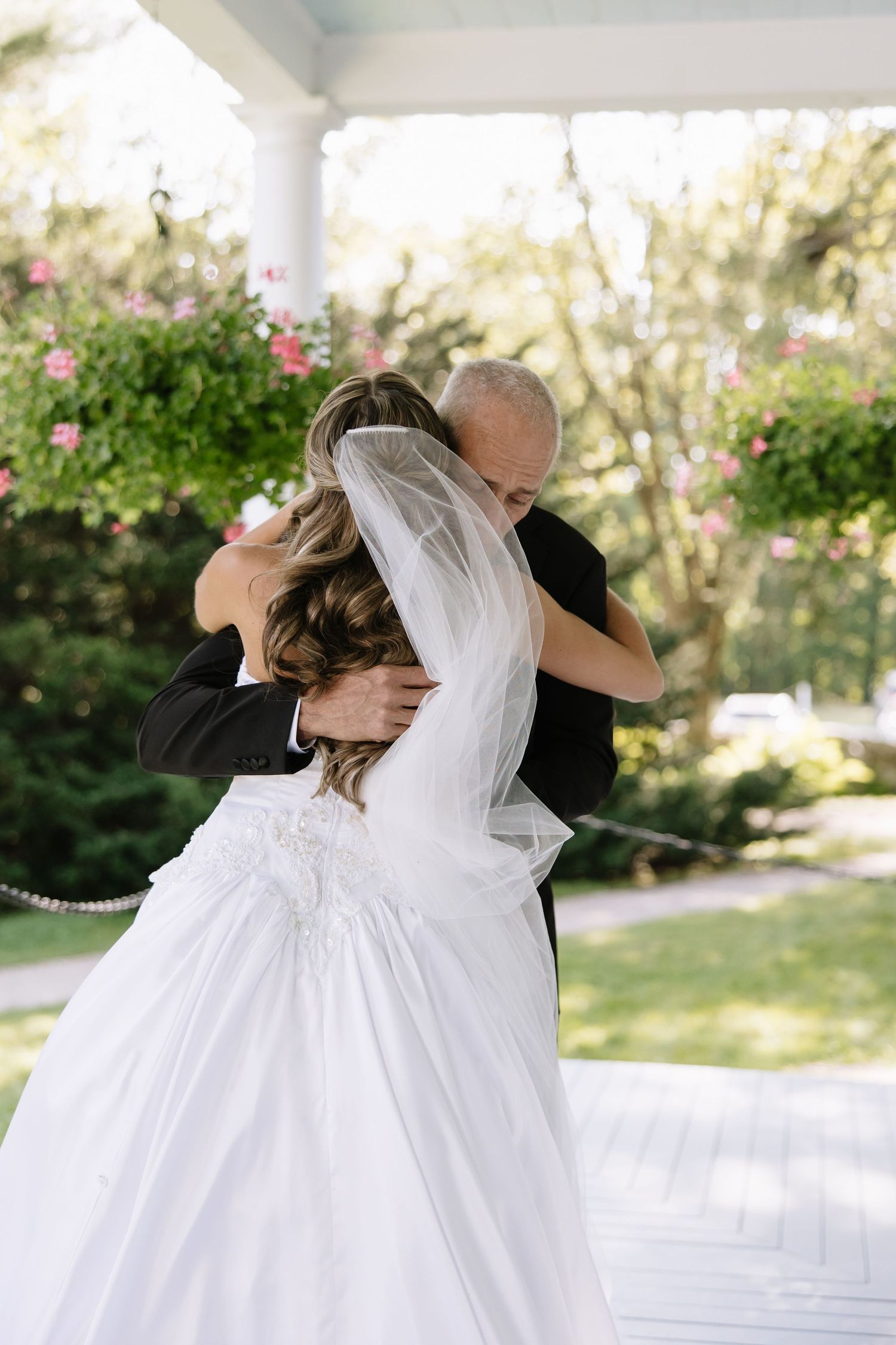 Elegant wedding couple embracing on white columned porch with flowing bridal gown.