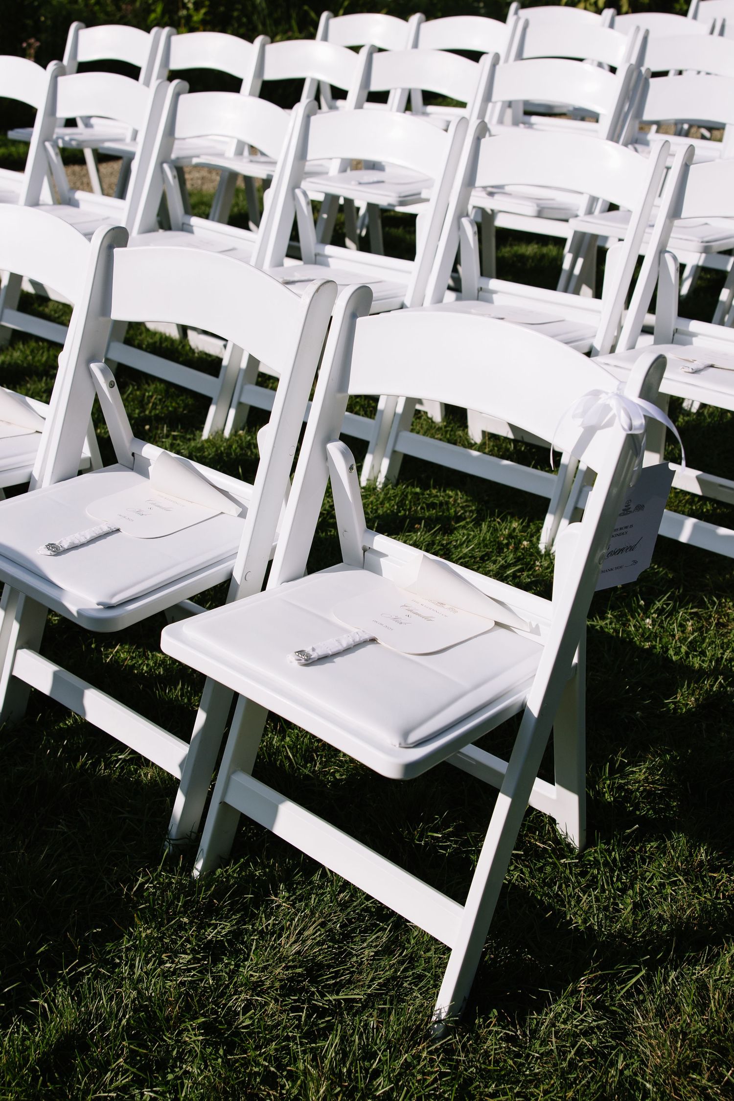 Rows of white folding chairs arranged on grass for an outdoor wedding ceremony.